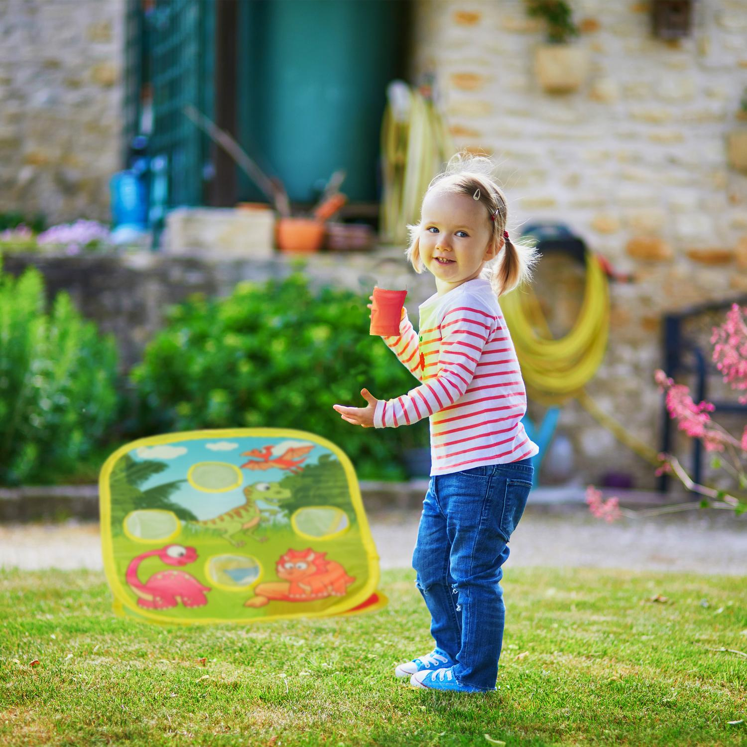 Una niña juega en el jardín con un juego de lanzar bolsas de dinosaurios.
