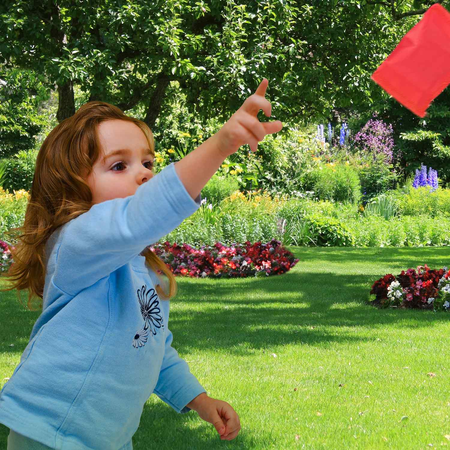Una niña con camiseta azul lanza un objeto rojo en un jardín.