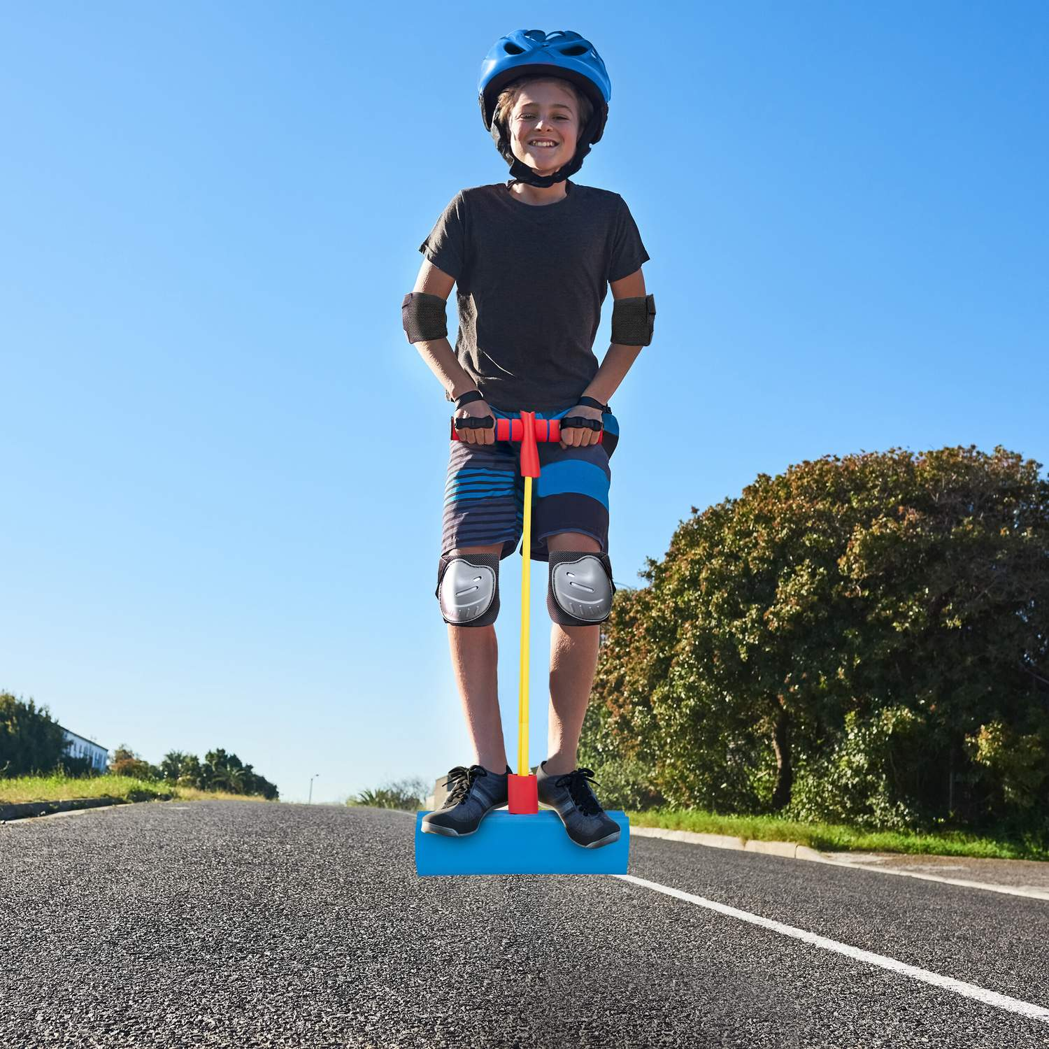 Niño con casco y equipo de protección en un pogo stick azul en una carretera.