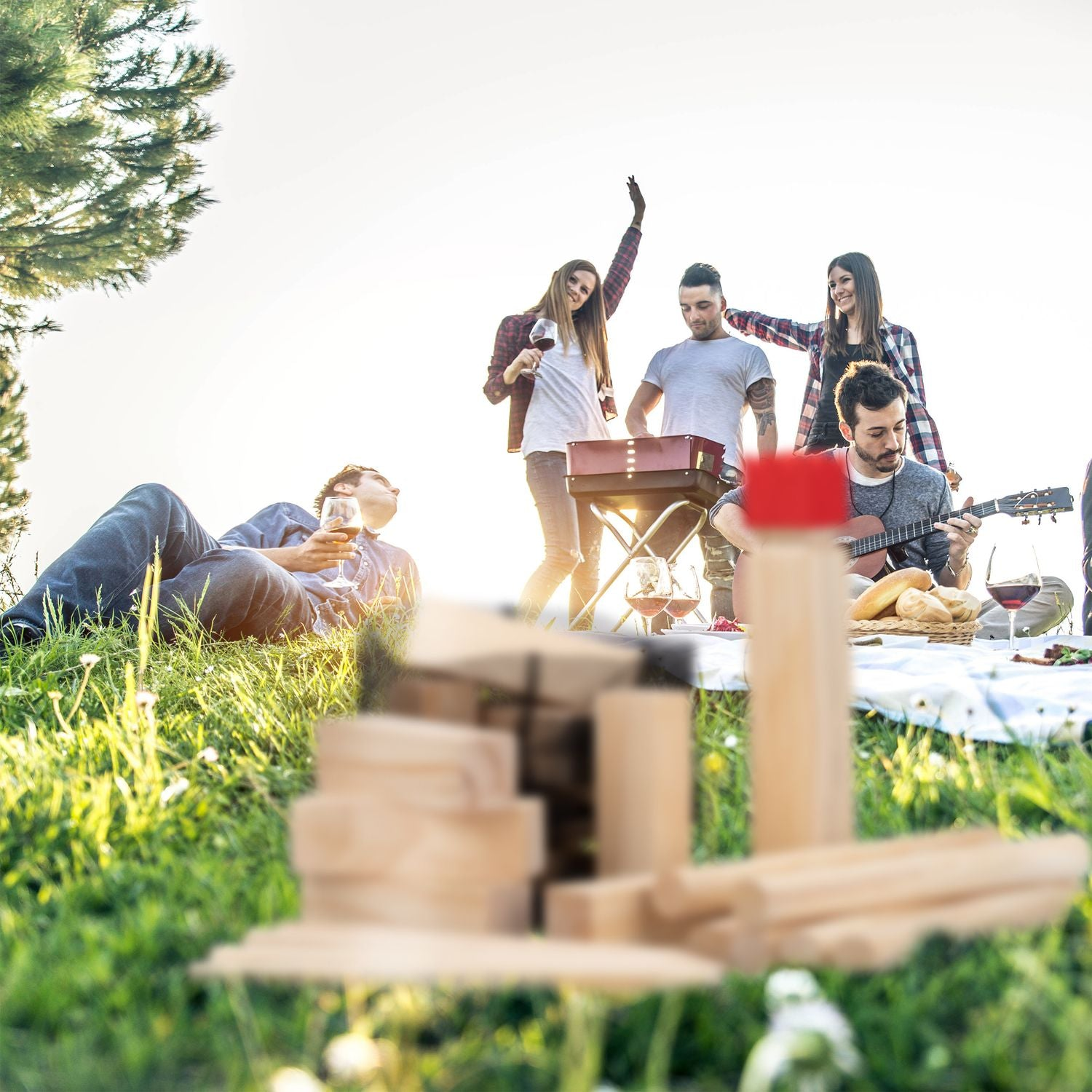 Amigos hacen barbacoa y tocan guitarra en un prado soleado.