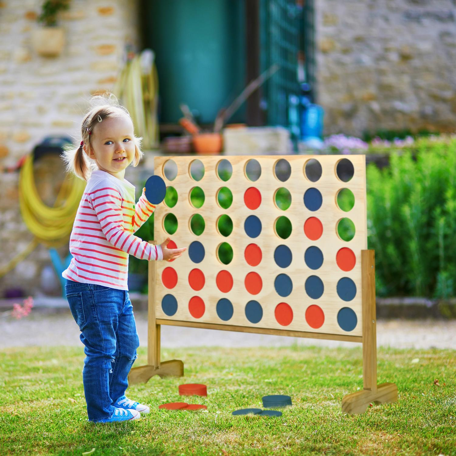 Niña pequeña juega Conecta 4 en un jardín con discos rojos y azules.