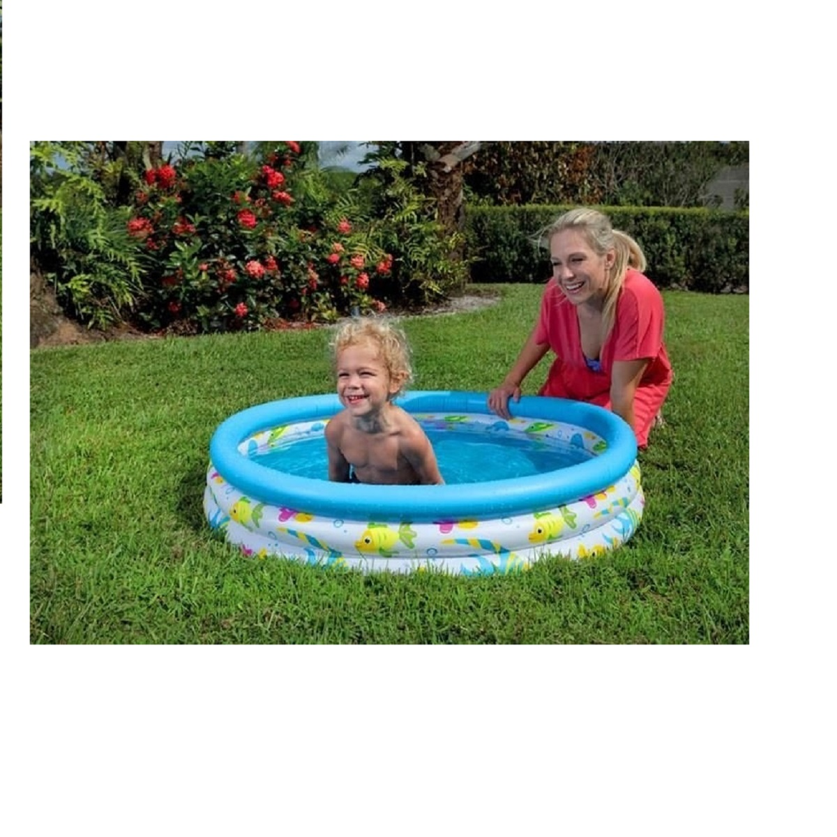 Un niño pequeño con cabello rizado sonríe sentado en una piscina inflable azul y blanca, junto a una mujer arrodillada.