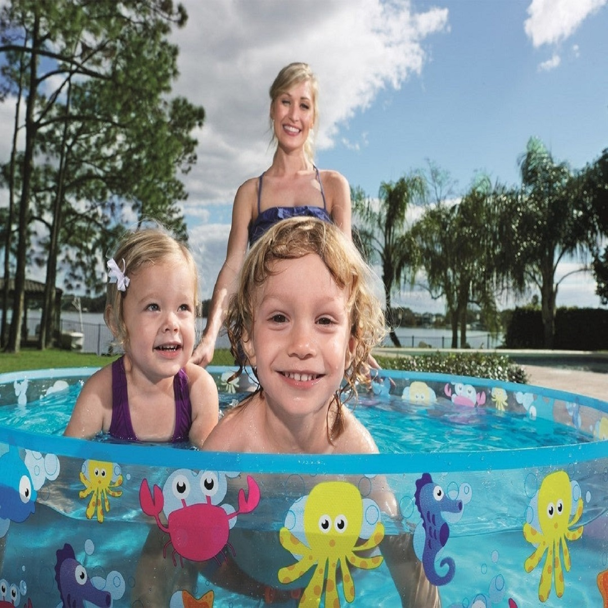 Una mujer con dos niños chapoteando en una piscina inflable con diseños de criaturas marinas.