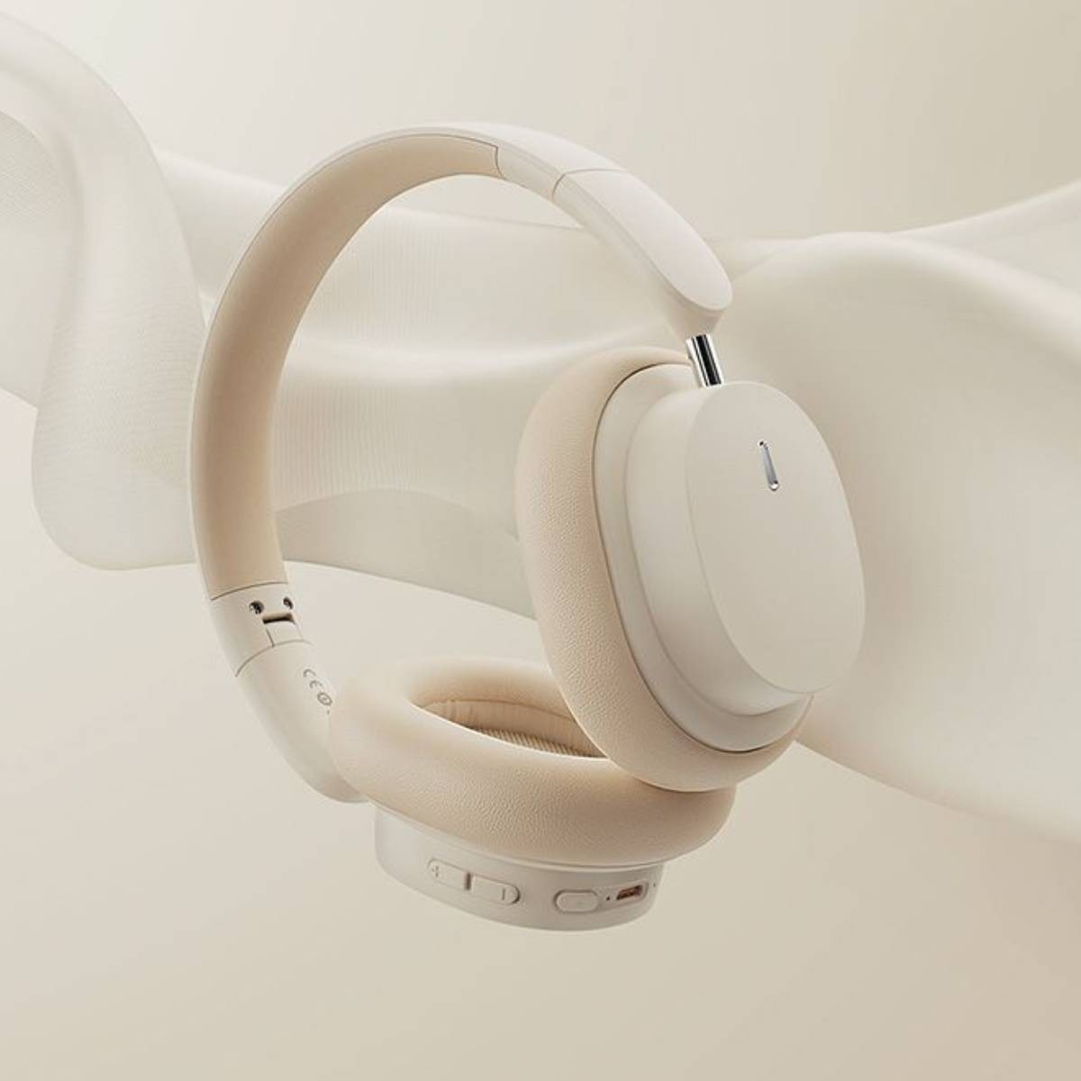 Auriculares color crema con diadema y almohadillas suaves sobre fondo de tela color crema.