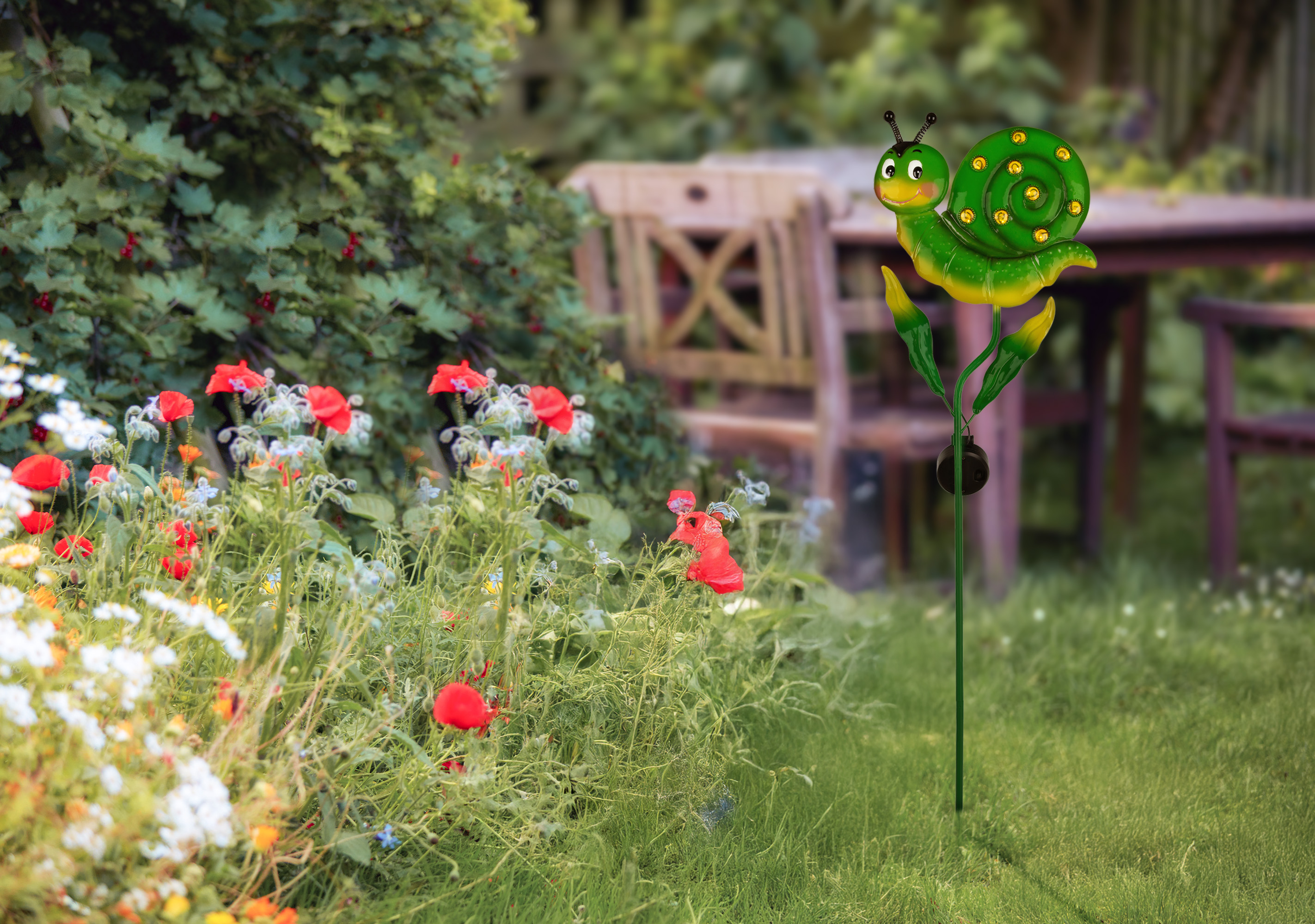 Ein grüner Schneckengartendekor steht im Gras neben Blumen und einem Tisch.
