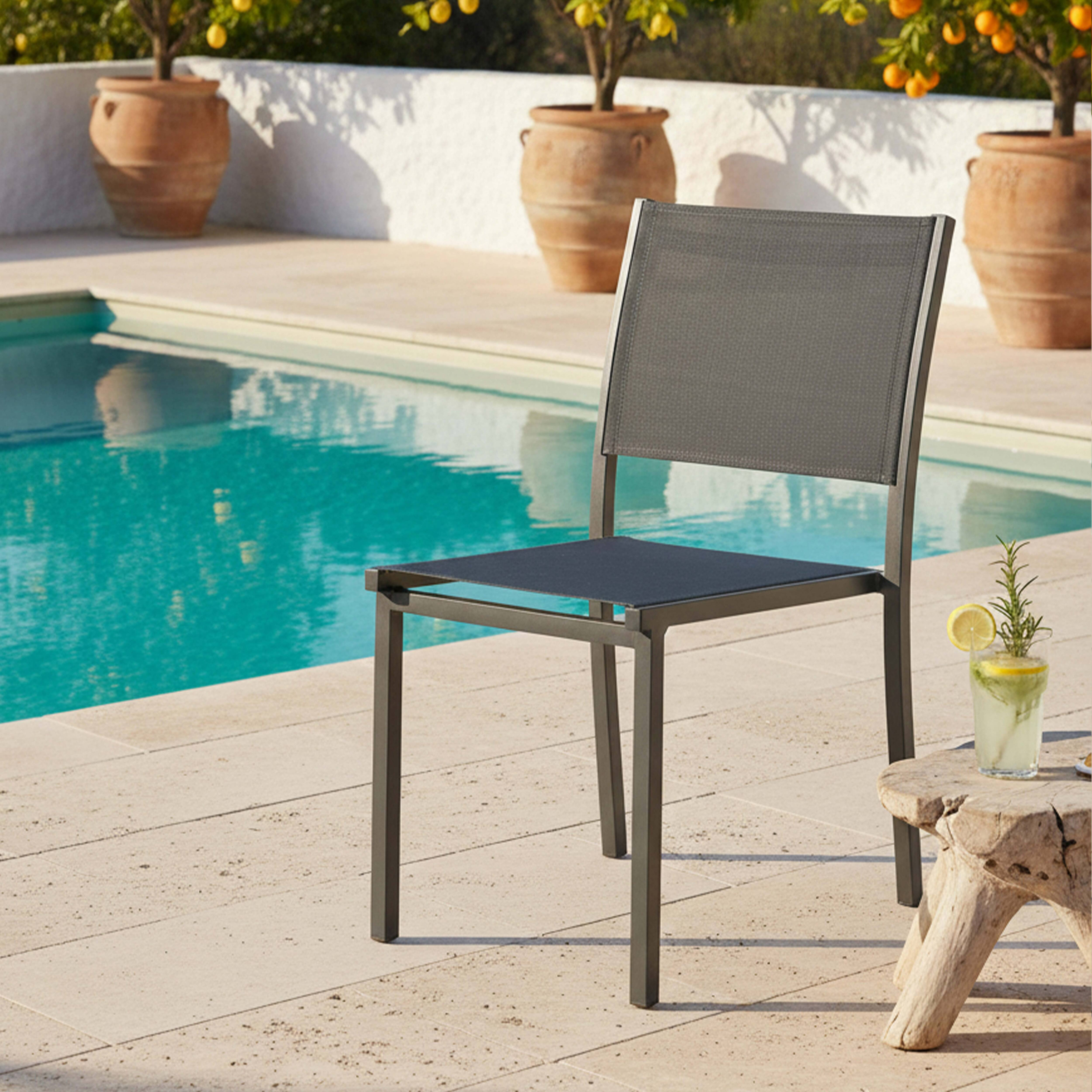 Ein grauer Stuhl neben einem Pool mit einem Getränk auf einem Holztisch.