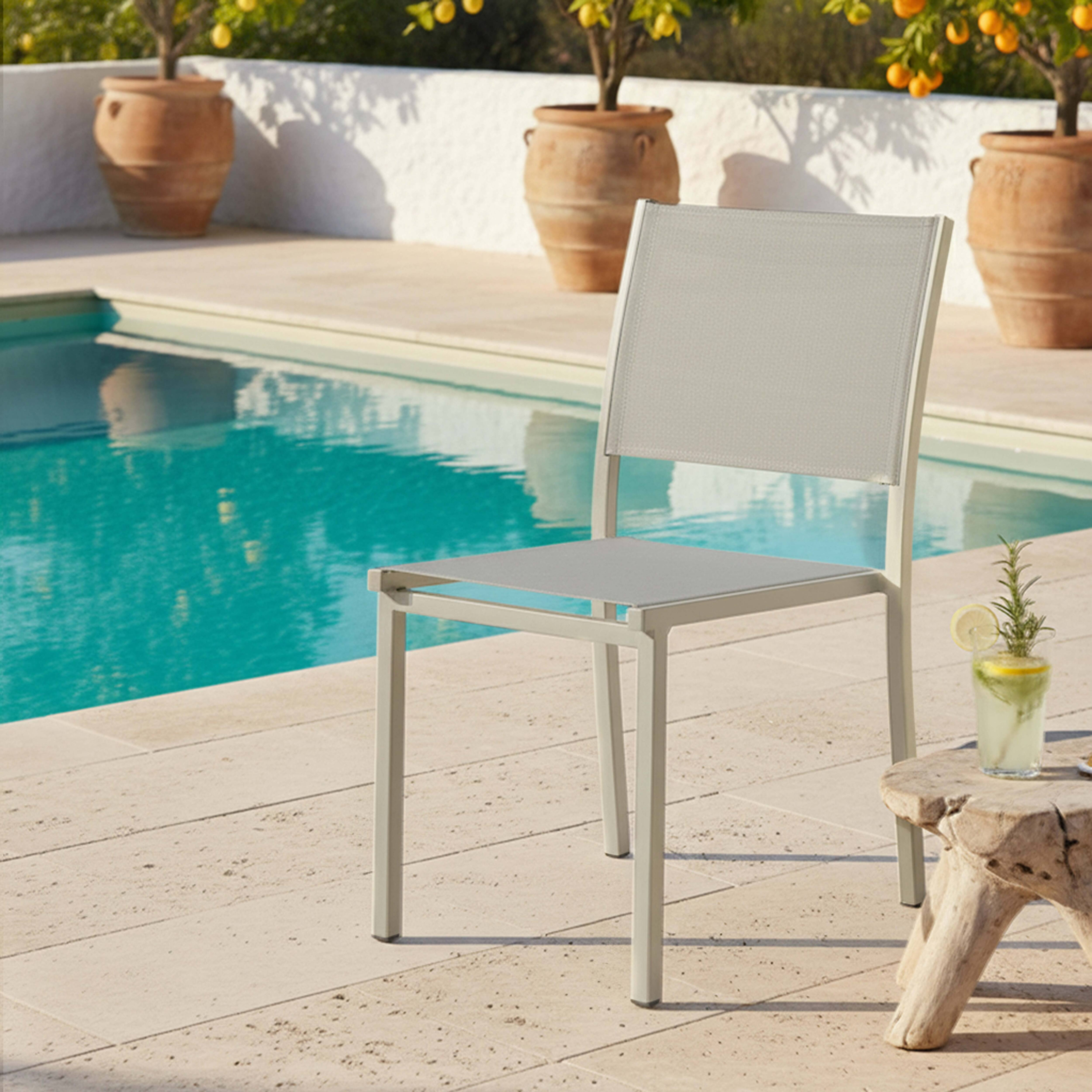 Ein heller Stuhl am Pool mit Orangenbäumen und Terrakottatöpfen.