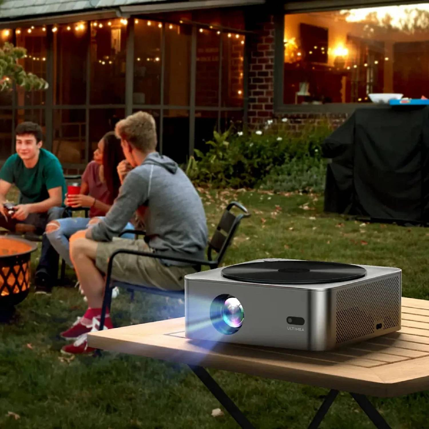 Projektor na stole w ogrodzie, podczas gdy przyjaciele rozmawiają w tle.