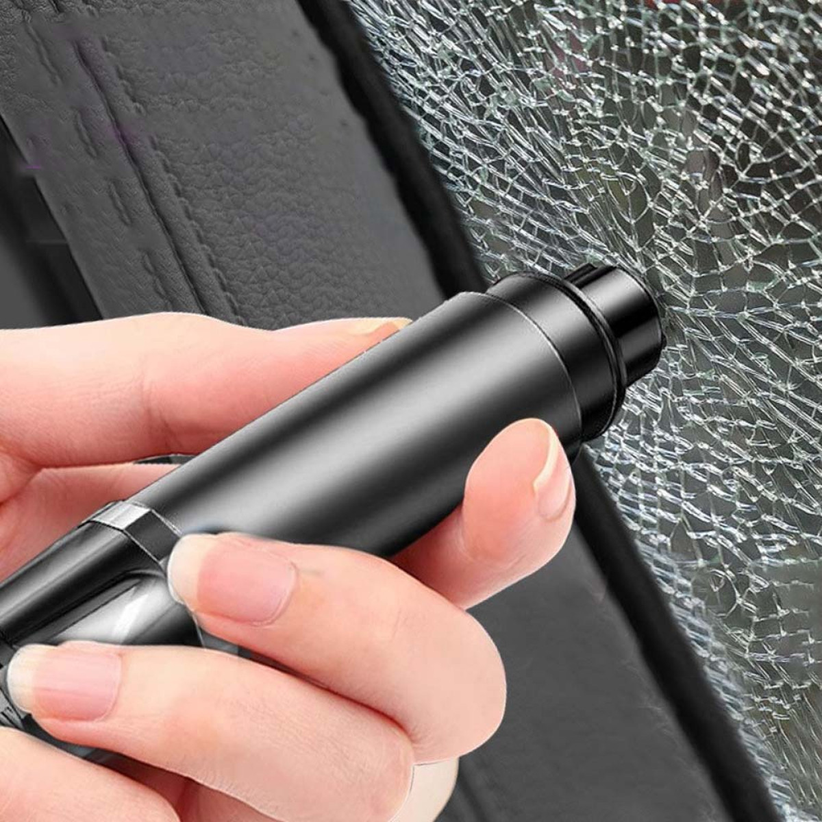 Ręka trzyma czarny wybijak do szyb na rozbitej szybie samochodu.