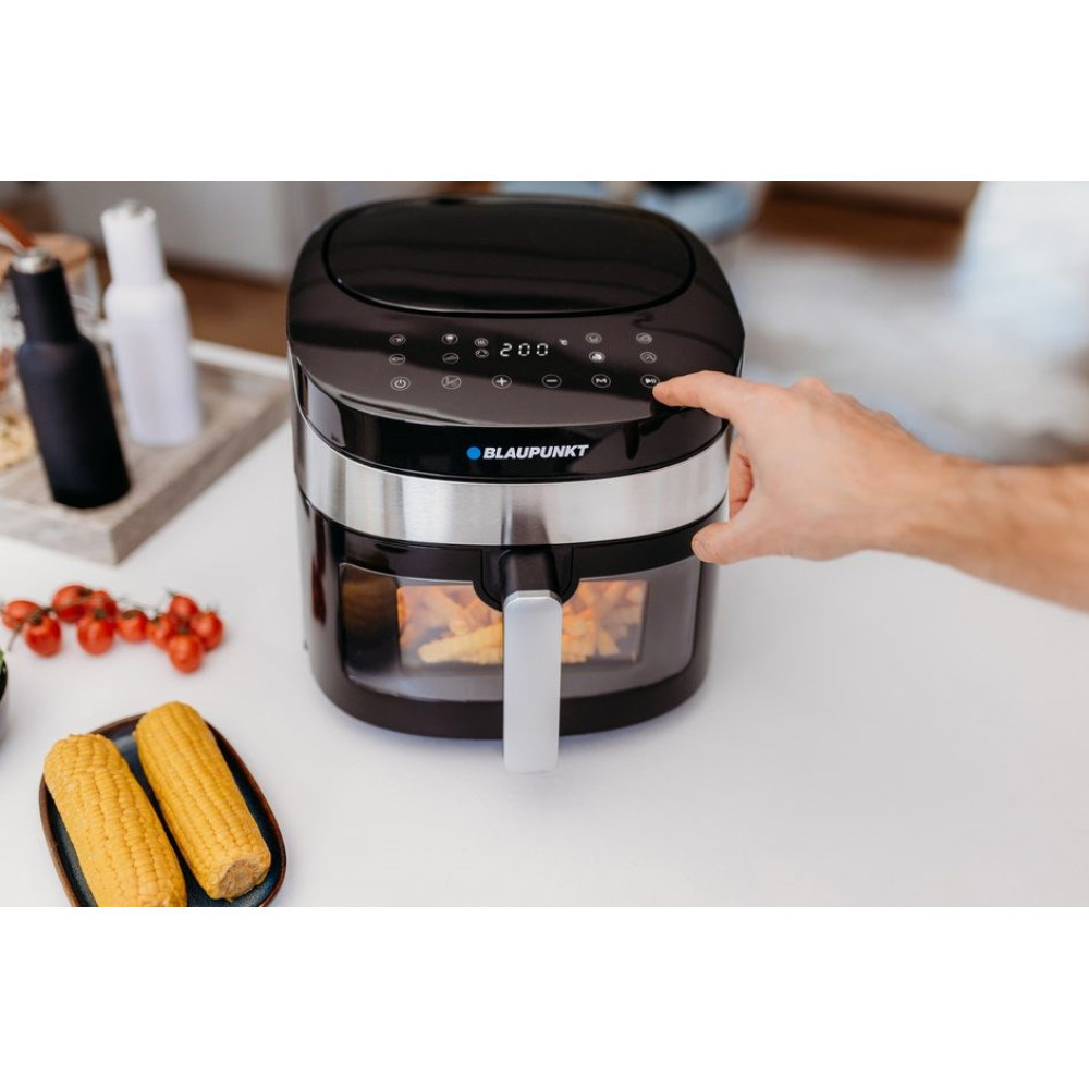 Czarna frytkownica beztłuszczowa z frytkami w środku. Ręka naciska przycisk.