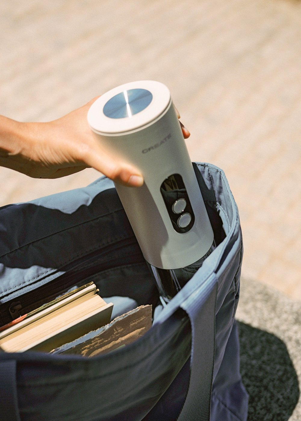 Una mano coloca un sacacorchos blanco en una bolsa azul con libros.