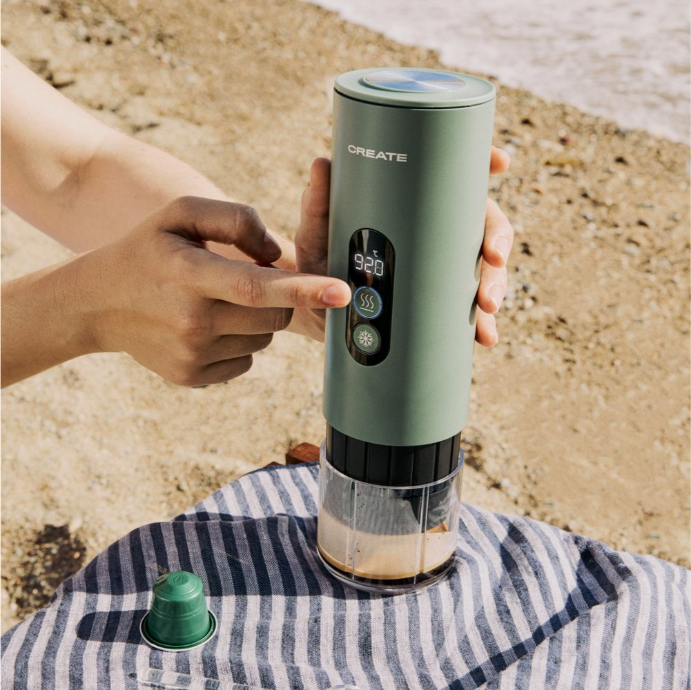 Dispositivo verde en toalla de playa, persona operándolo. Café en recipiente.