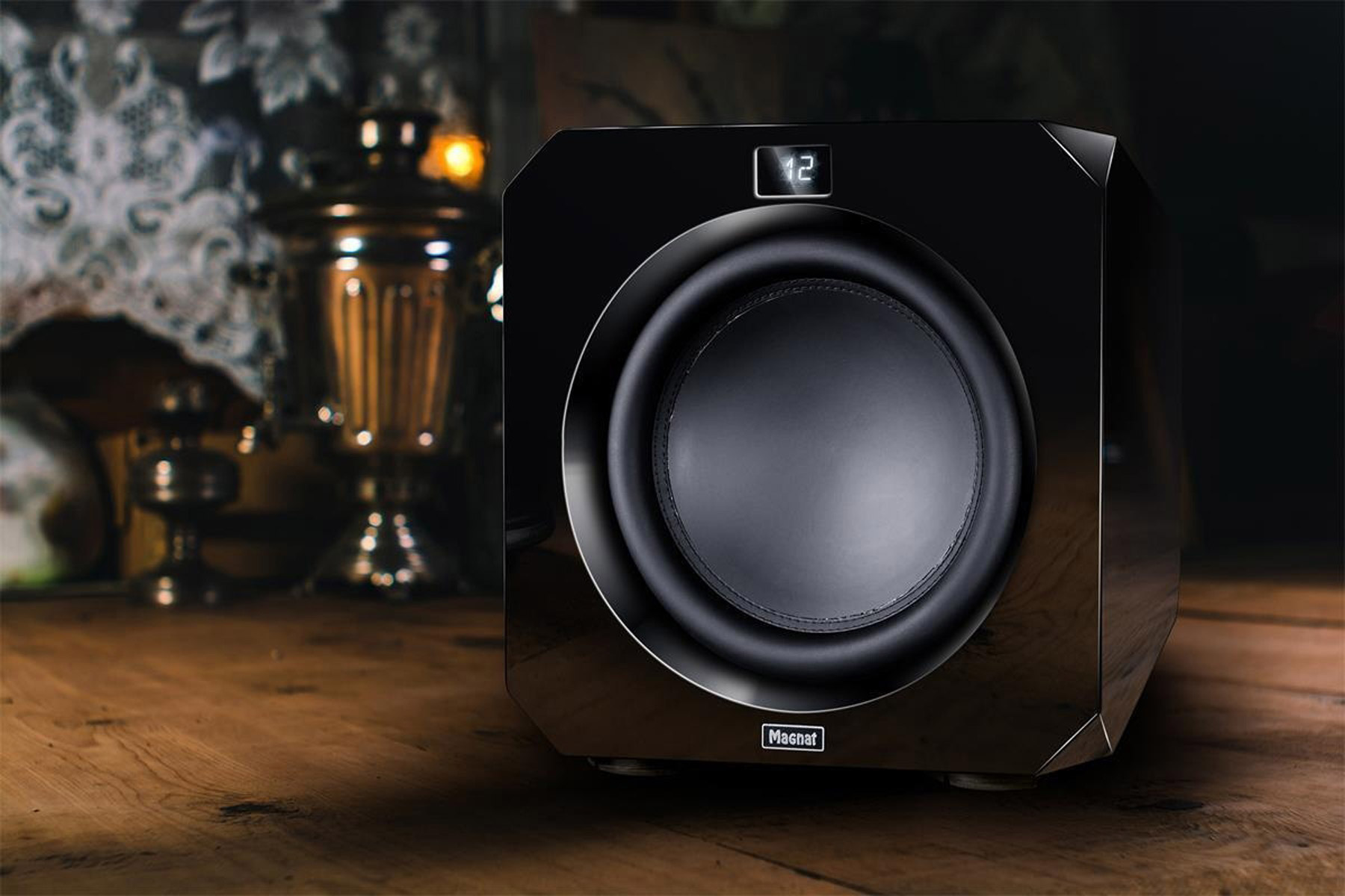 Schwarzer Subwoofer auf Holztisch, im Hintergrund ein Samowar.