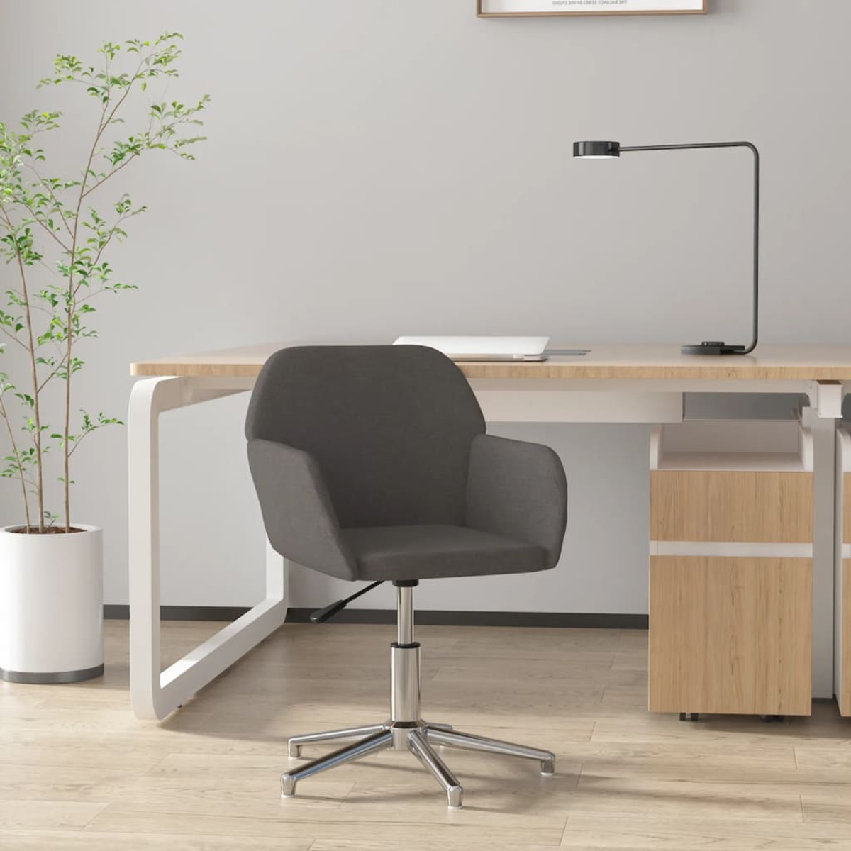 Ein dunkler Bürostuhl steht vor einem Schreibtisch mit einem Laptop und einer Lampe.