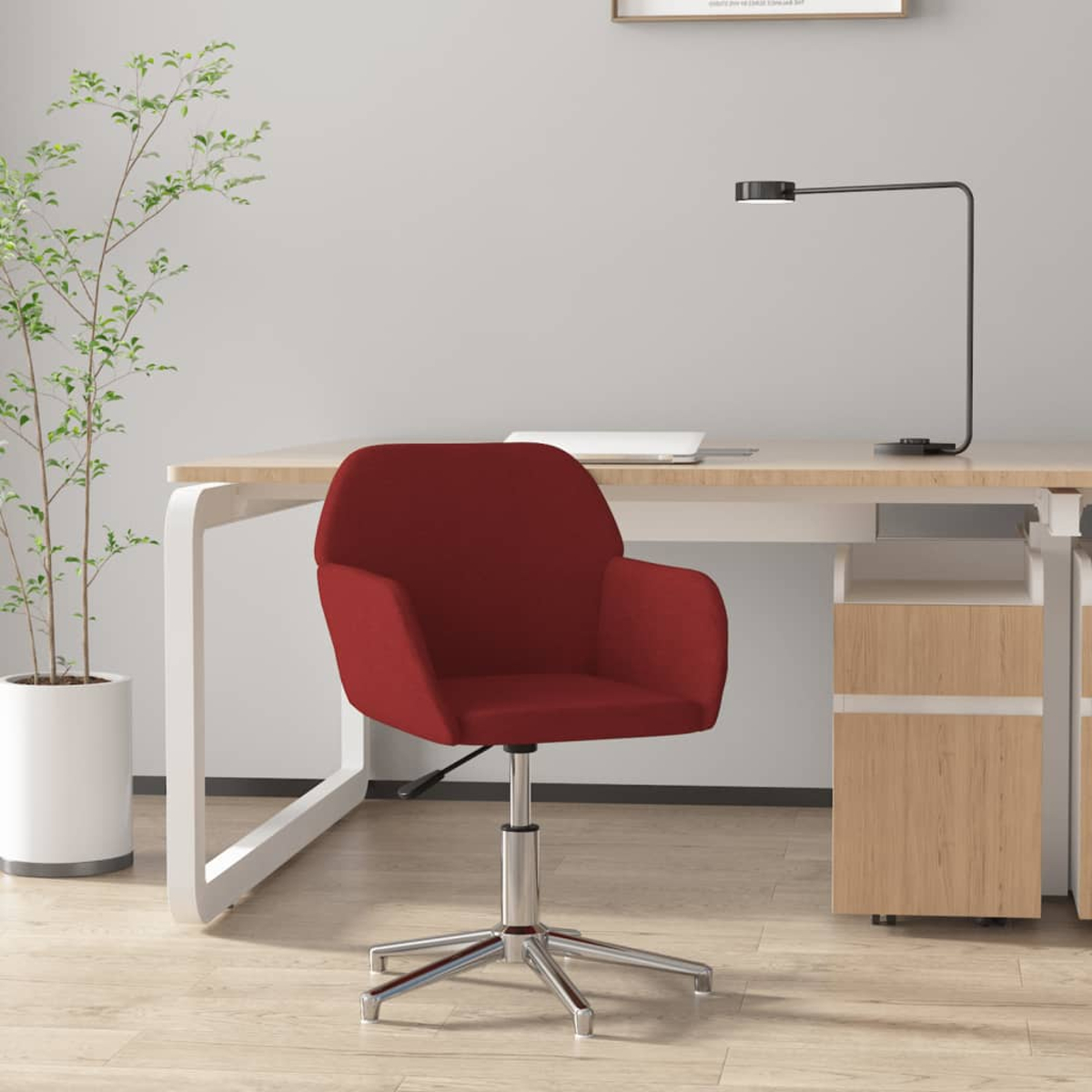 Ein roter Bürostuhl mit silbernem Fuß steht vor einem Schreibtisch mit einer Lampe.