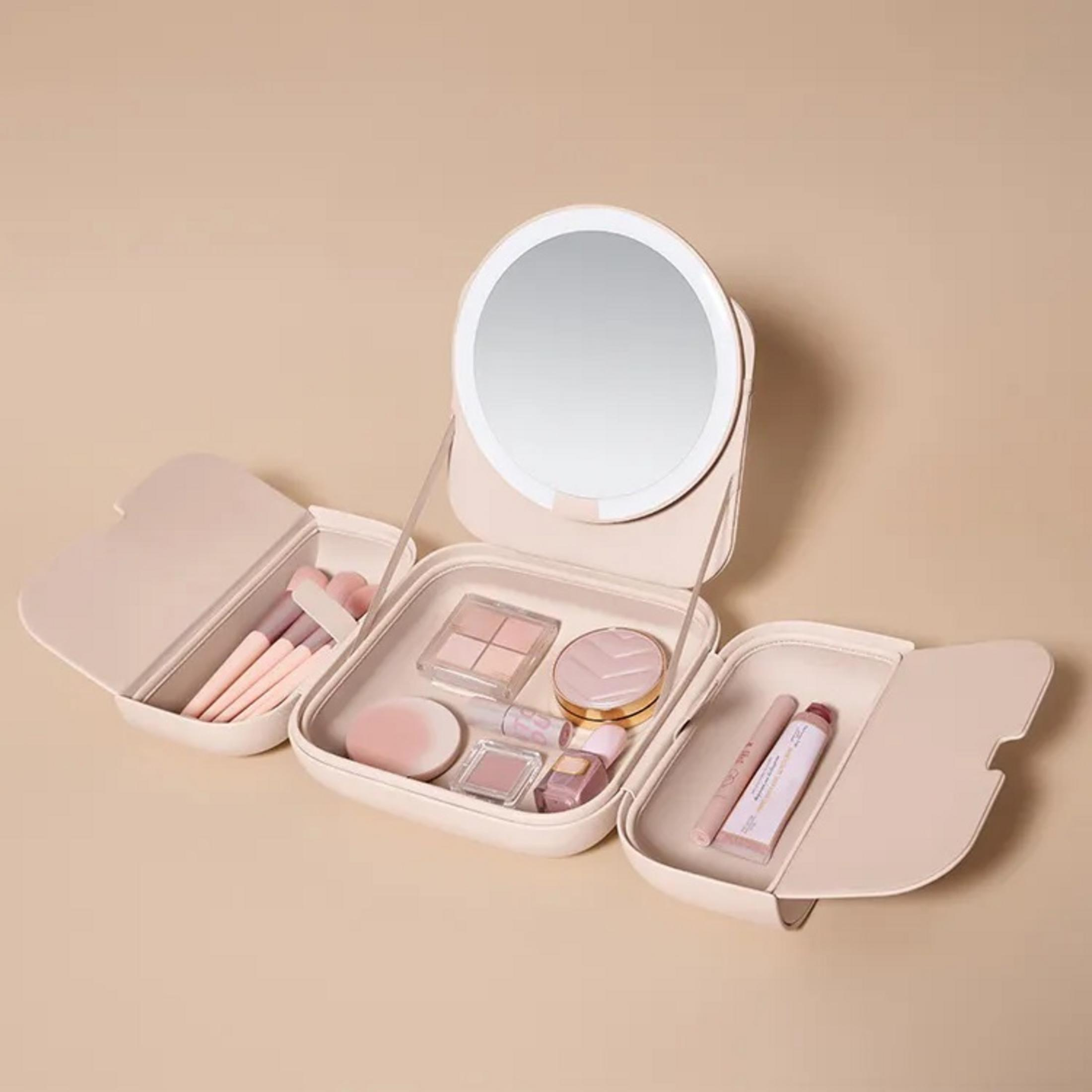 Un beauty case aperto con specchio, pennelli, ombretto, rossetto su sfondo beige.