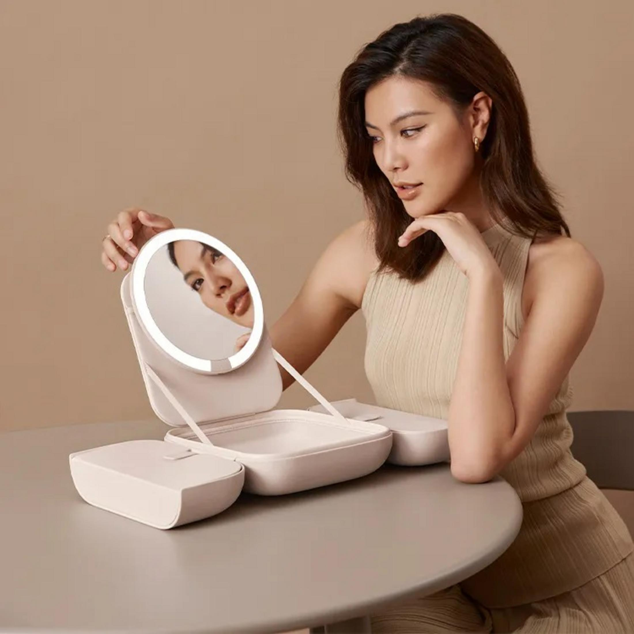 Una donna guarda uno specchio da trucco illuminato su un tavolo.