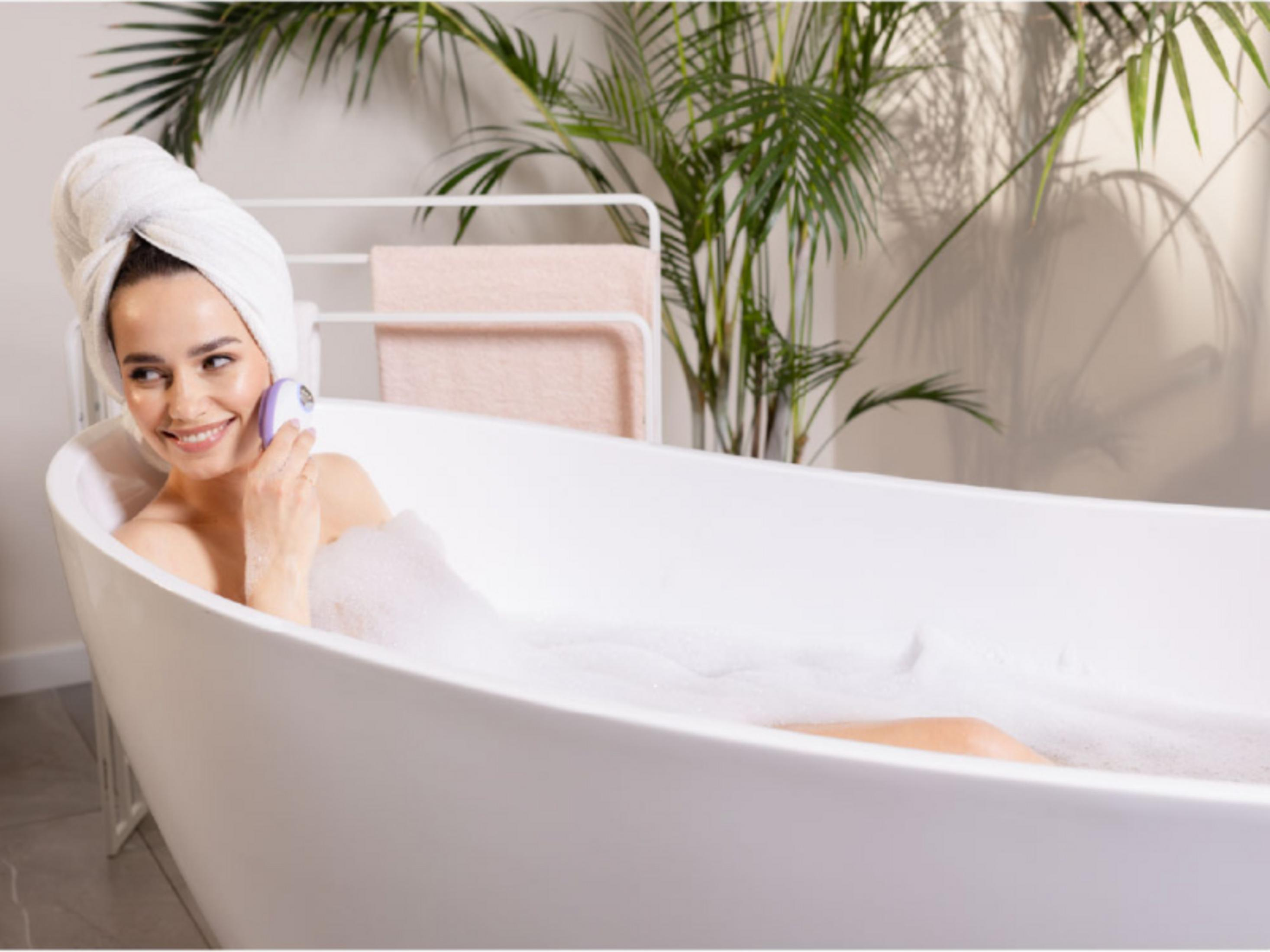 Donna in vasca da bagno con asciugamano e massaggiatore.
