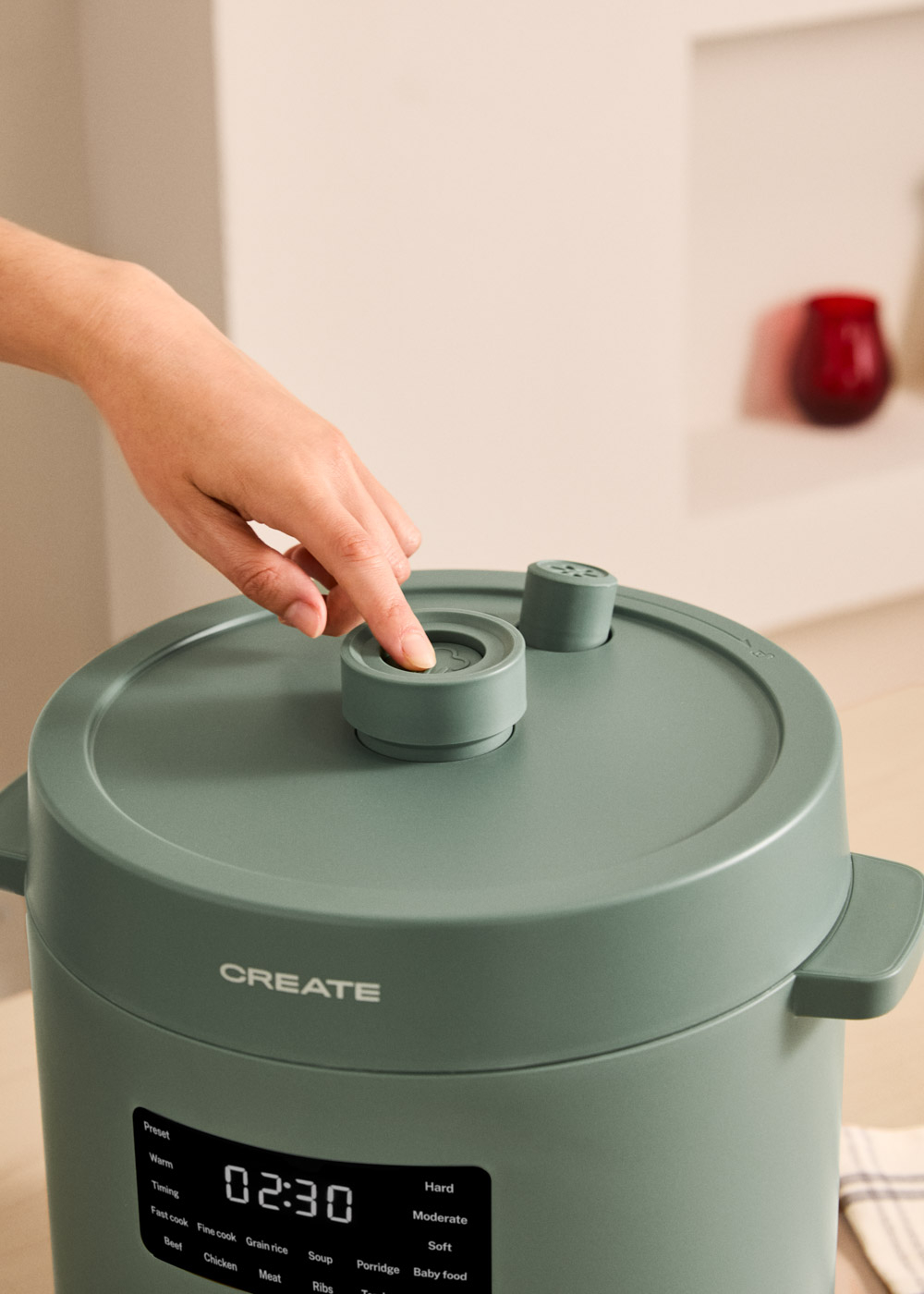 Una mano presiona el botón de una olla de cocina verde con pantalla digital.