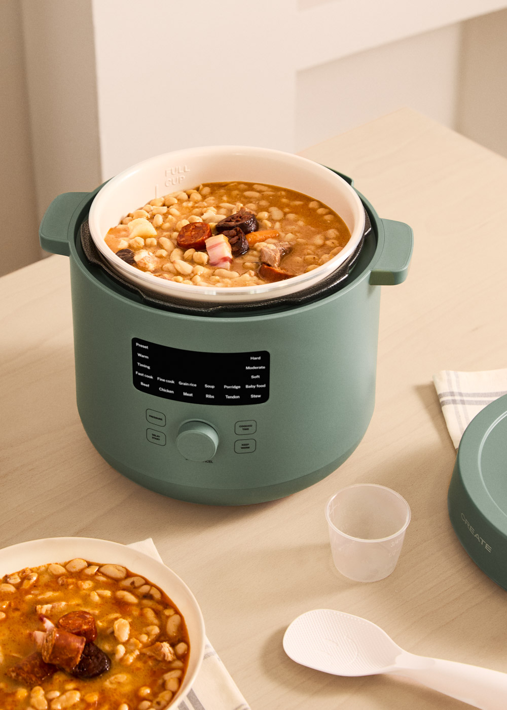 Una olla de cocción lenta verde con una olla interior llena de frijoles y carne.