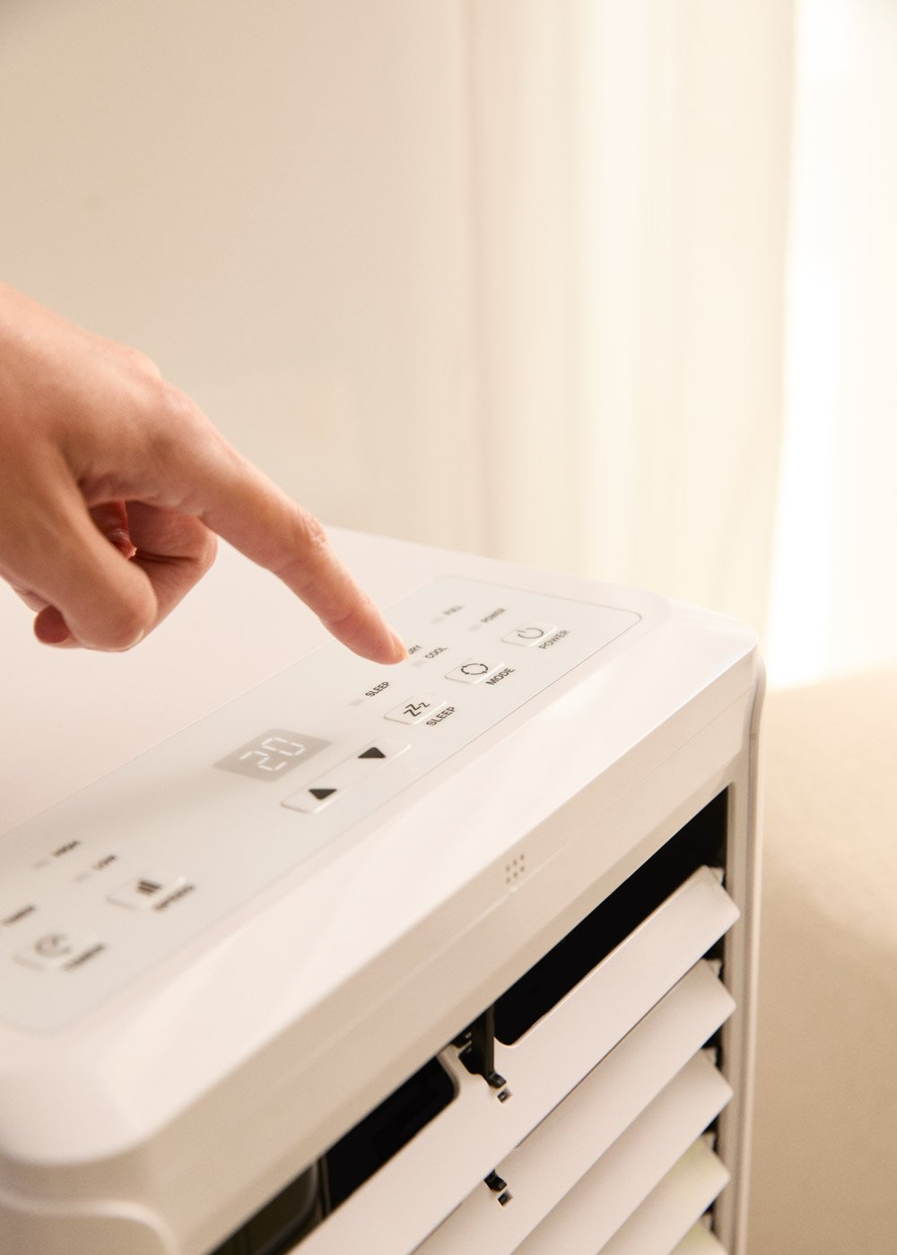 Una mano presiona un botón en un aire acondicionado blanco con pantalla digital.