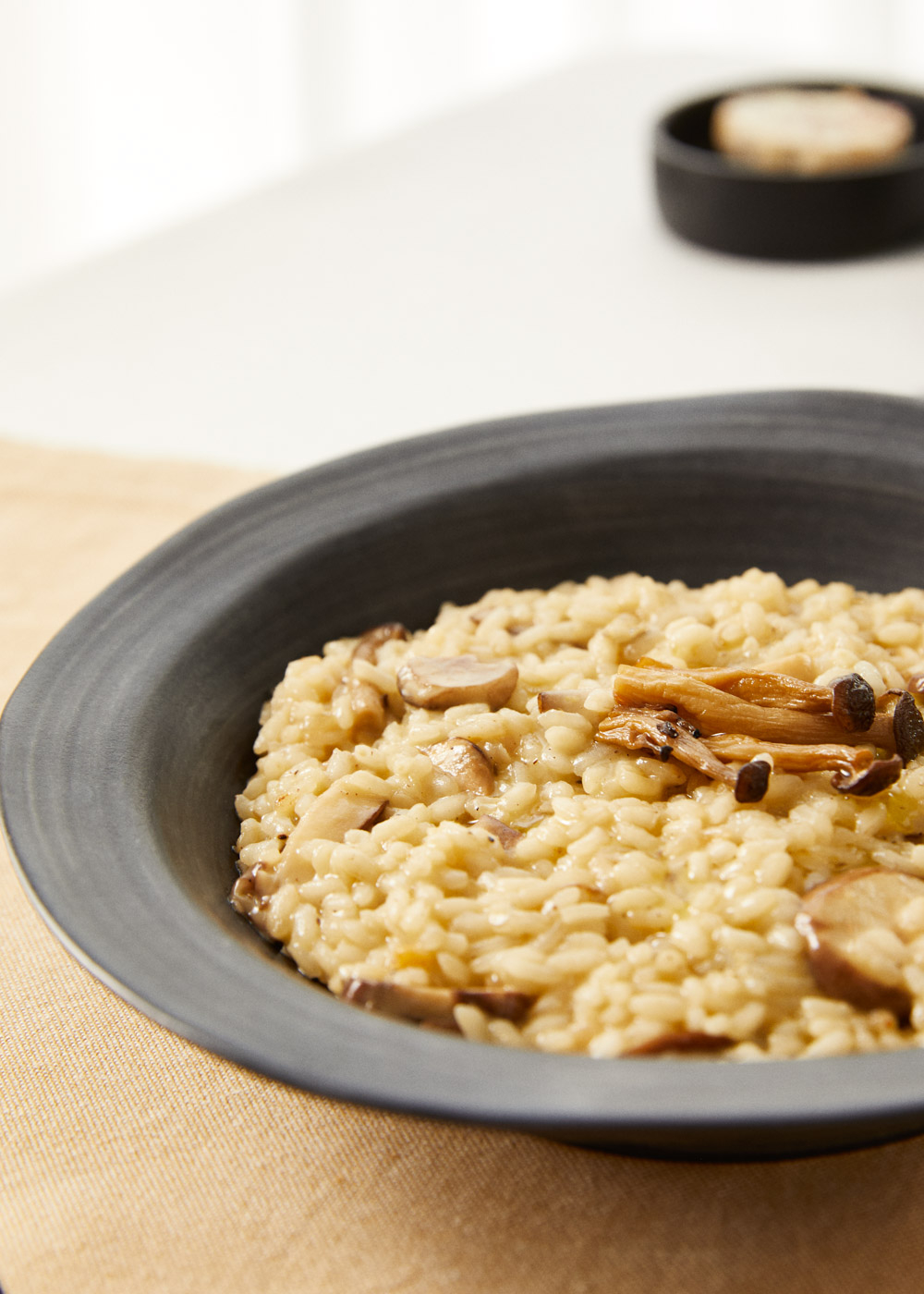 Risotto de champiñones en un cuenco oscuro sobre tela clara.