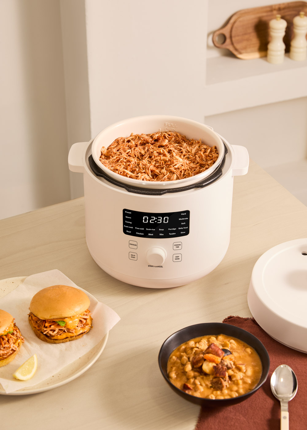 Una olla de cocción lenta blanca con pollo desmenuzado, hamburguesas y estofado cerca.