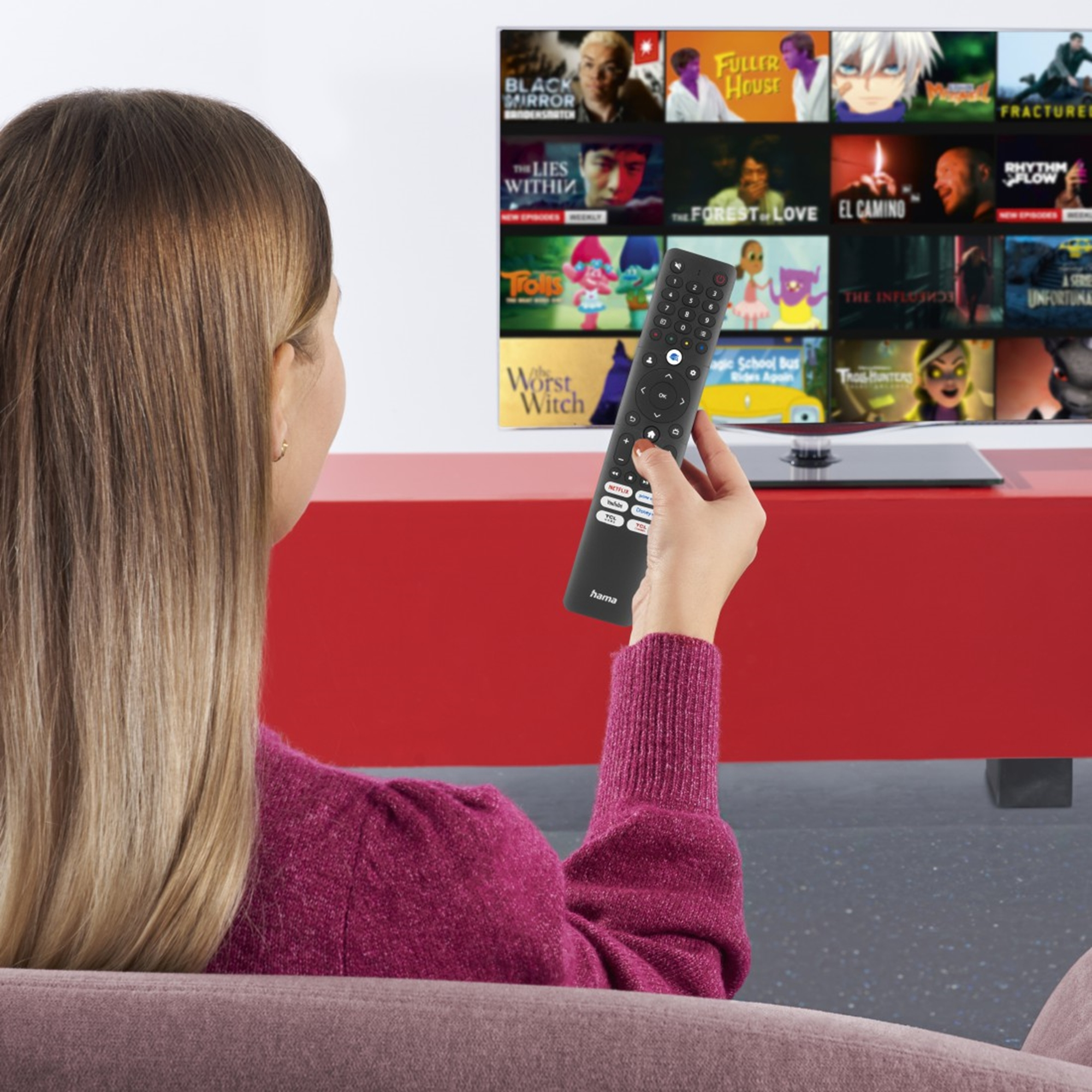 Eine Frau hält eine Fernbedienung und schaut auf einen Fernsehbildschirm mit Filmplakaten.