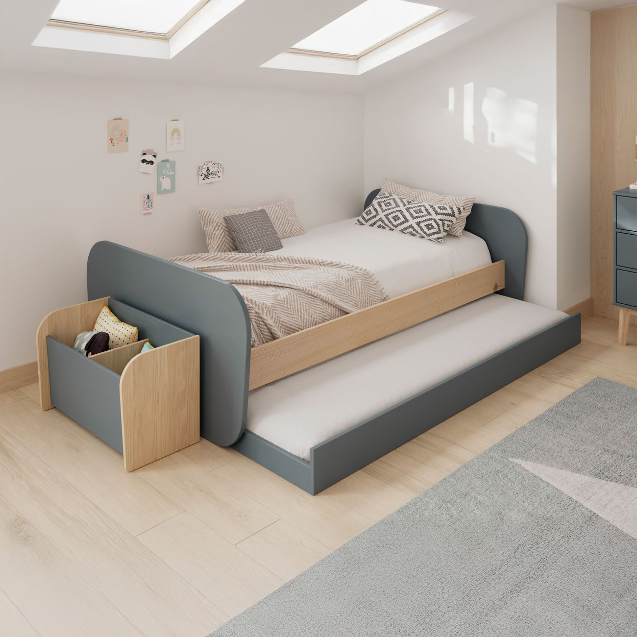 Una cama infantil azul con cama nido extraíble y caja de juguetes de madera.