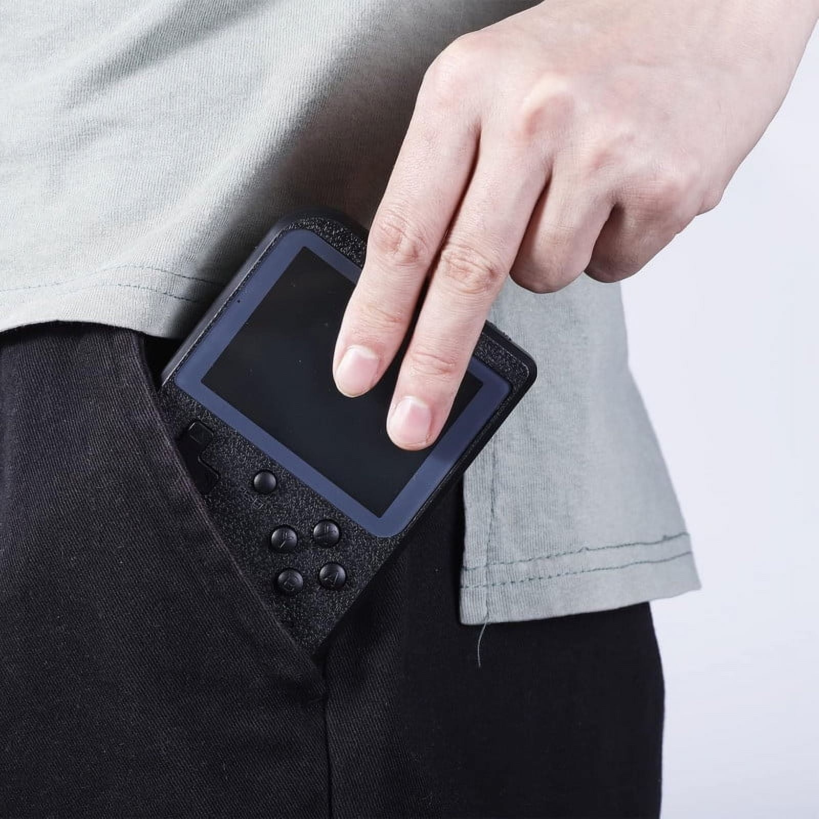 Hand steckt ein schwarzes Handheld-Spielgerät in eine Hosentasche.