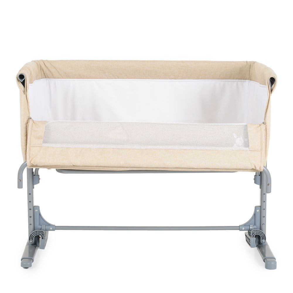 Ein beiger Babybeistellbett mit weißer Innenauskleidung und Gitter.