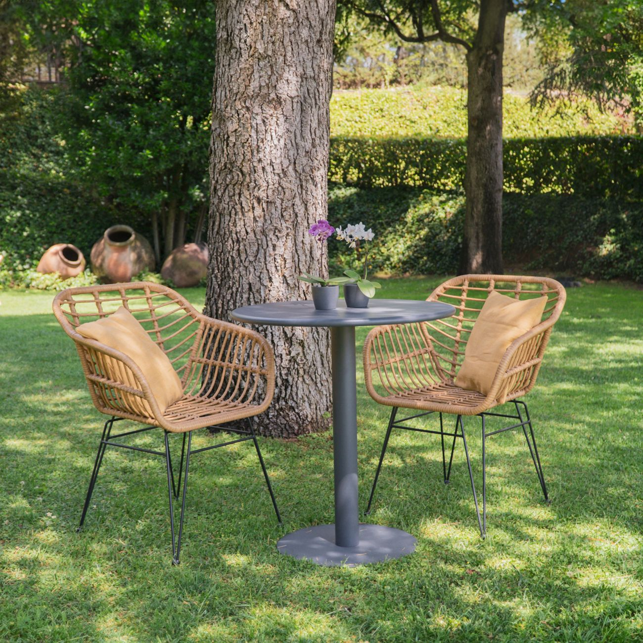 Dos sillas de mimbre con cojines se sientan ante una mesa en un jardín.
