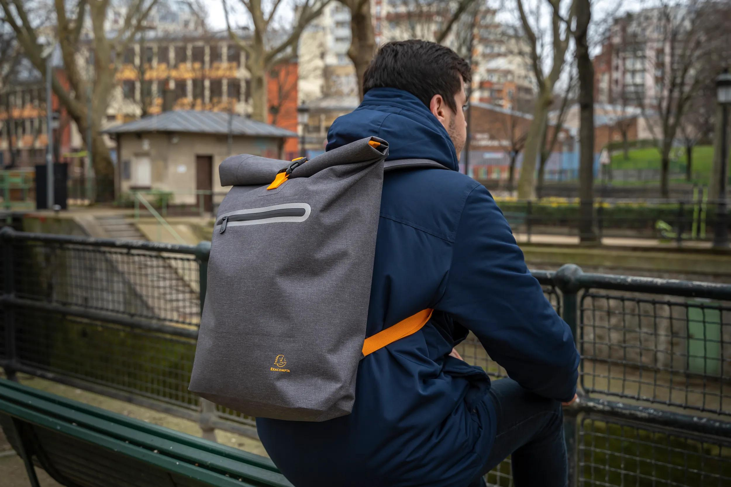 Mann mit grauem Rucksack und orangefarbenen Trägern sitzt auf einer Bank.