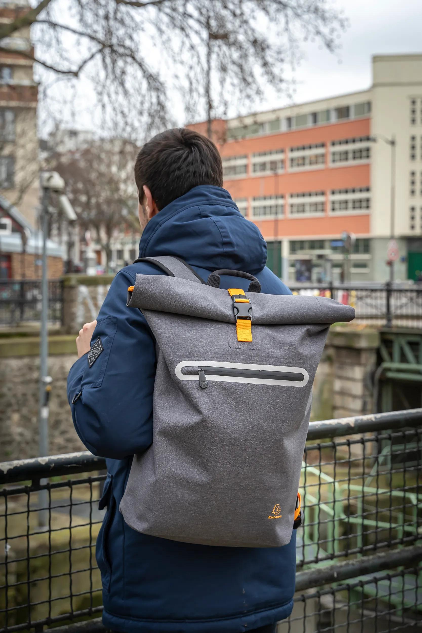 Mann mit grauem Rucksack und blauer Jacke steht draußen.