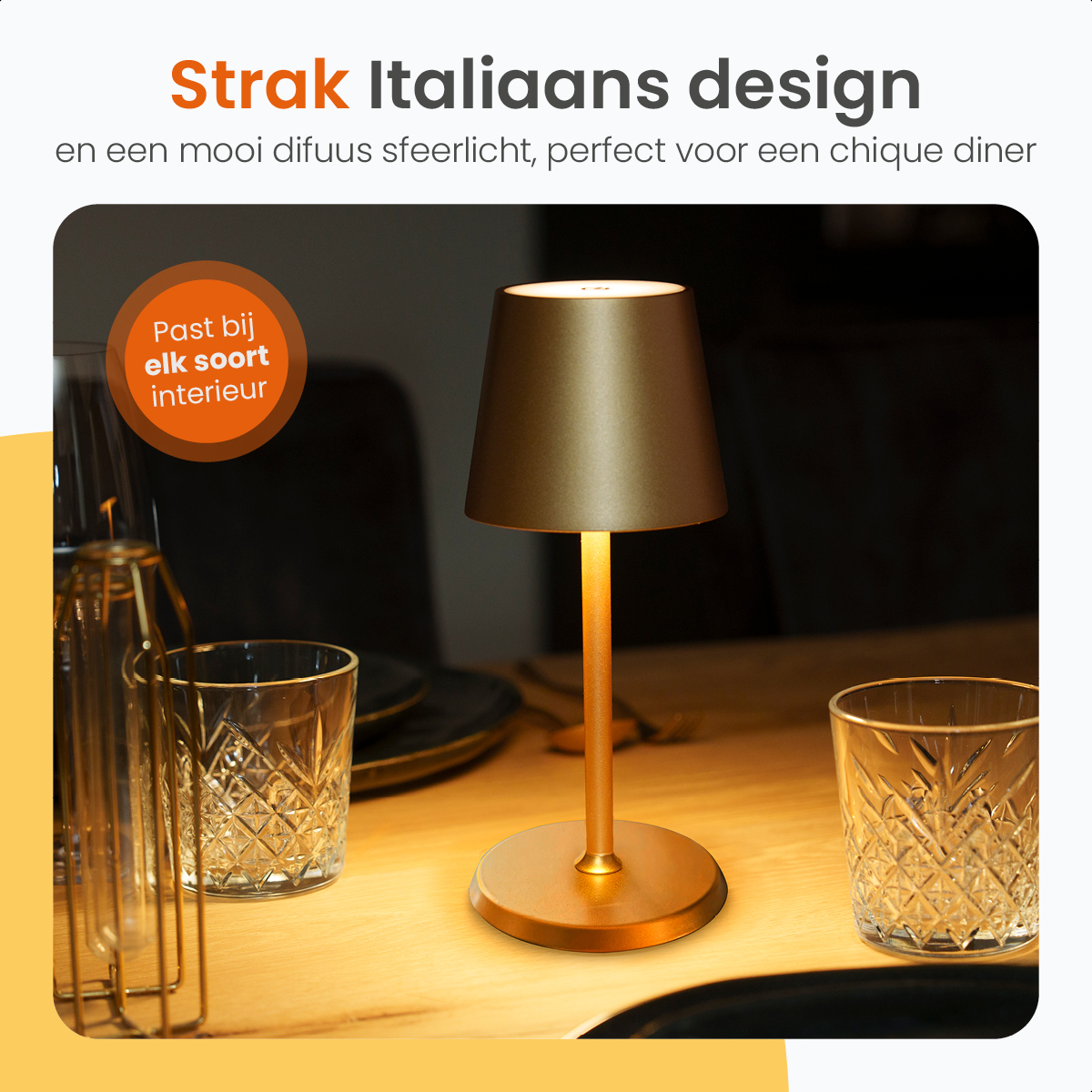 A golden table lamp with a lampshade on a wooden table next to glasses.