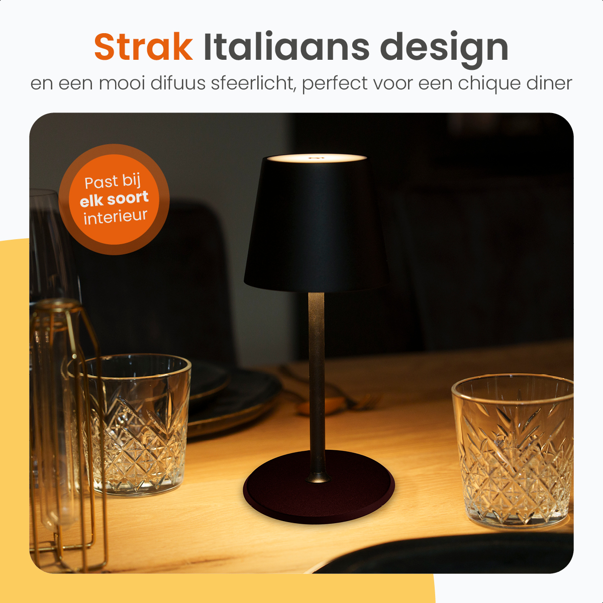 A black table lamp stands on a wooden table next to glasses.