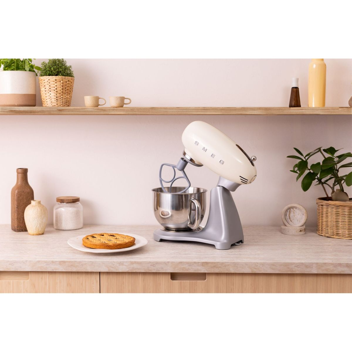 Gümüş tabanlı krem renkli SMEG stand mikseri, bir tartın yanında tezgahta duruyor.