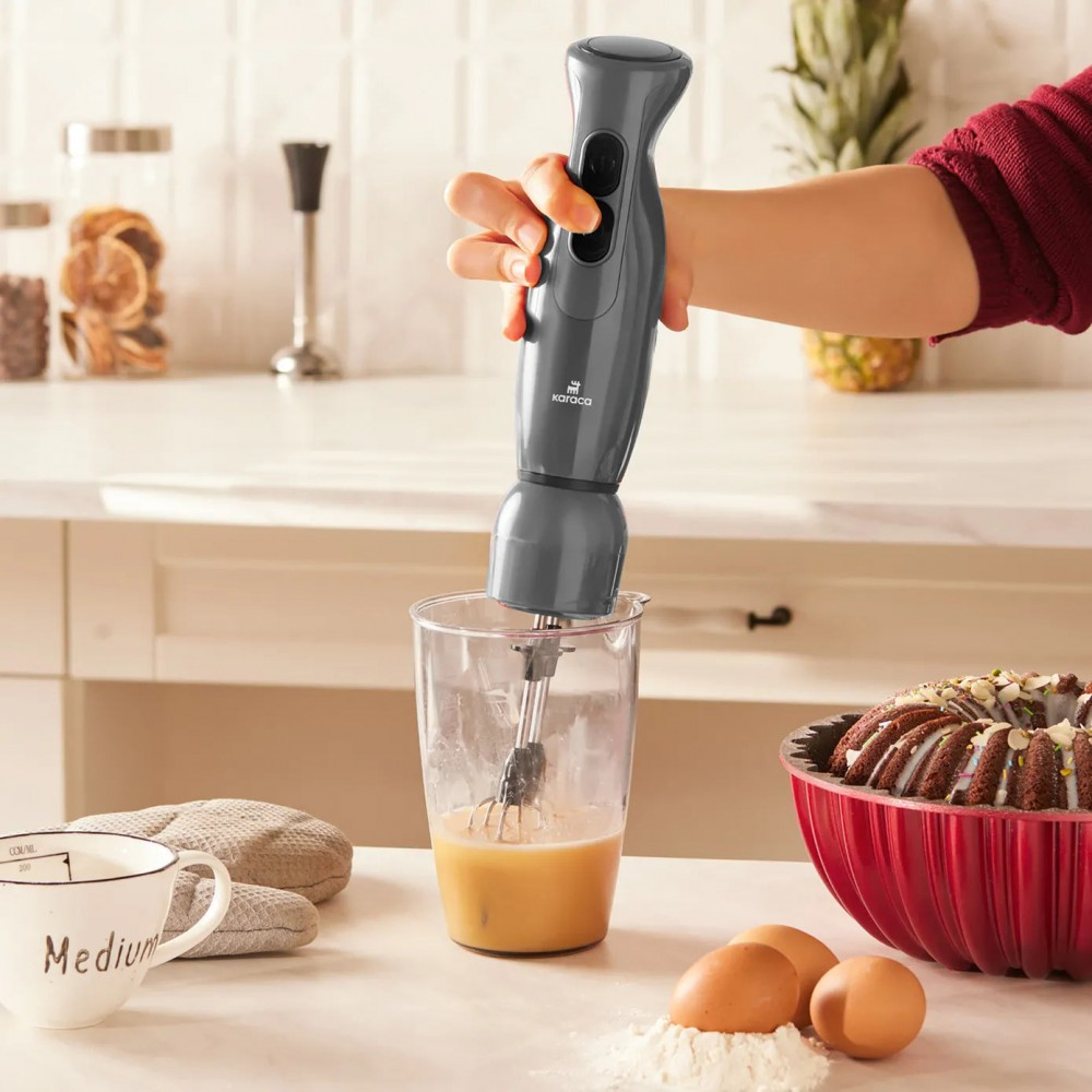 Gri el blender bardağı sarı sıvıyı karıştırıyor. Yanında kek ve yumurta.