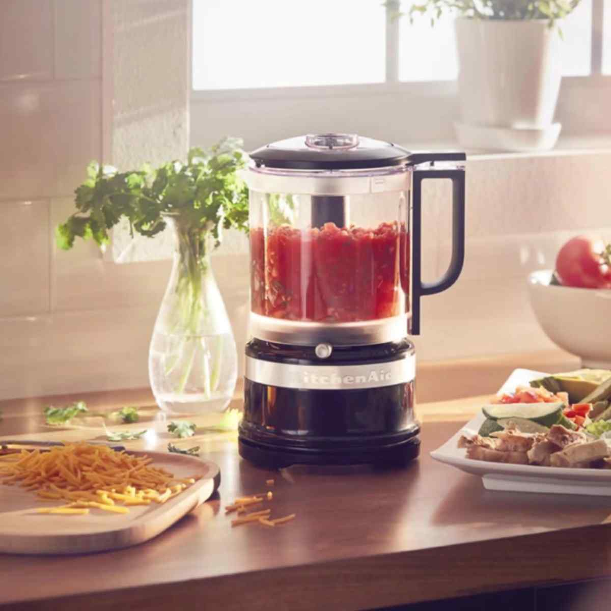 Domatesli mutfak robotu, rendelenmiş peynir ve tavuk salatasının yanında tezgahta duruyor.