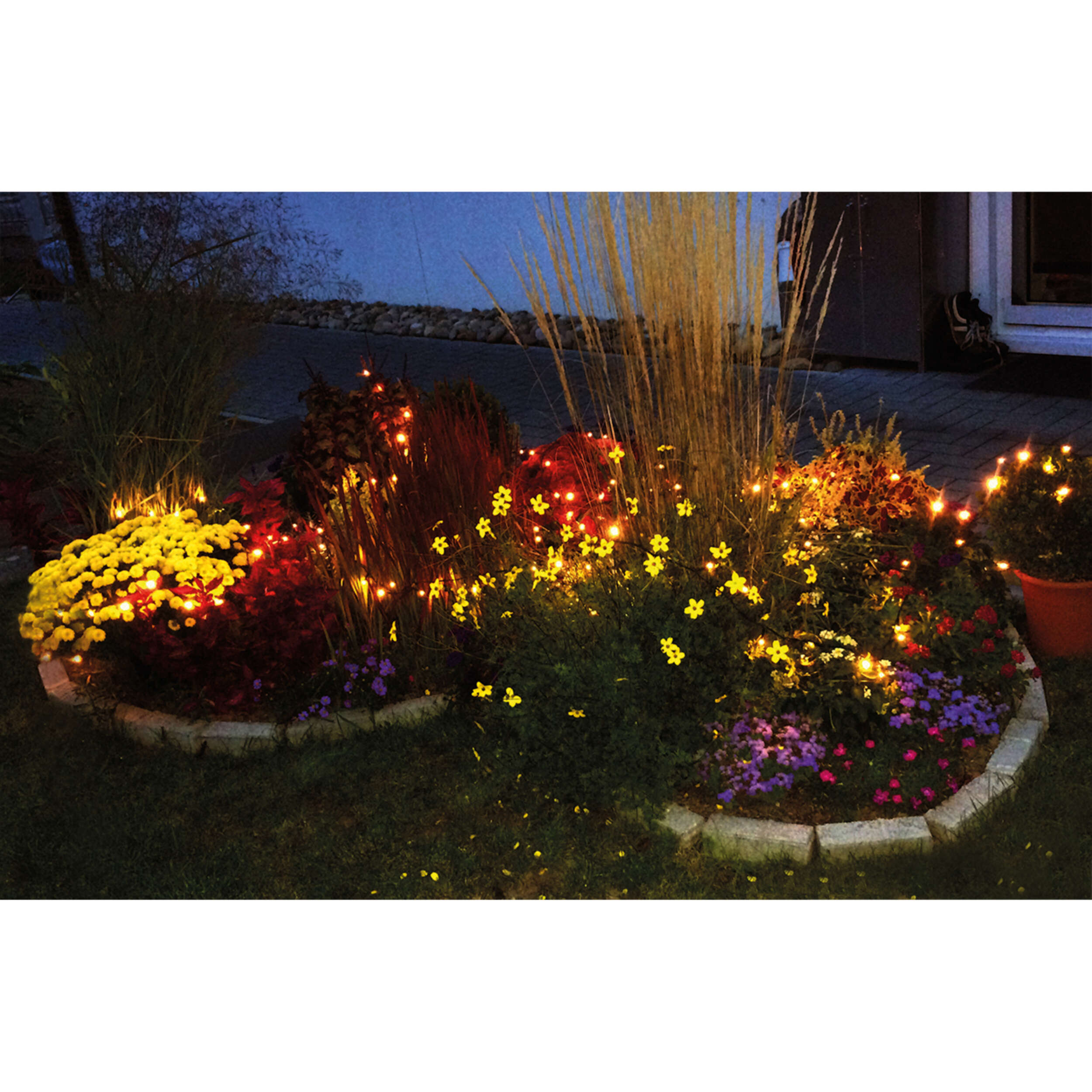 Ein Blumenbeet mit gelben und roten Blumen, geschmückt mit Lichterketten.