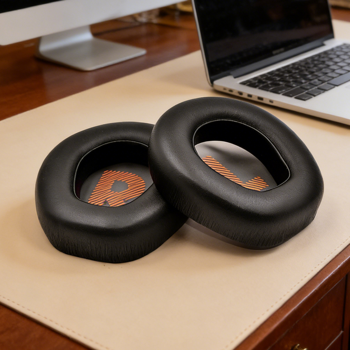 Dwa czarne nauszniki z pomarańczowym wzorem na biurku.