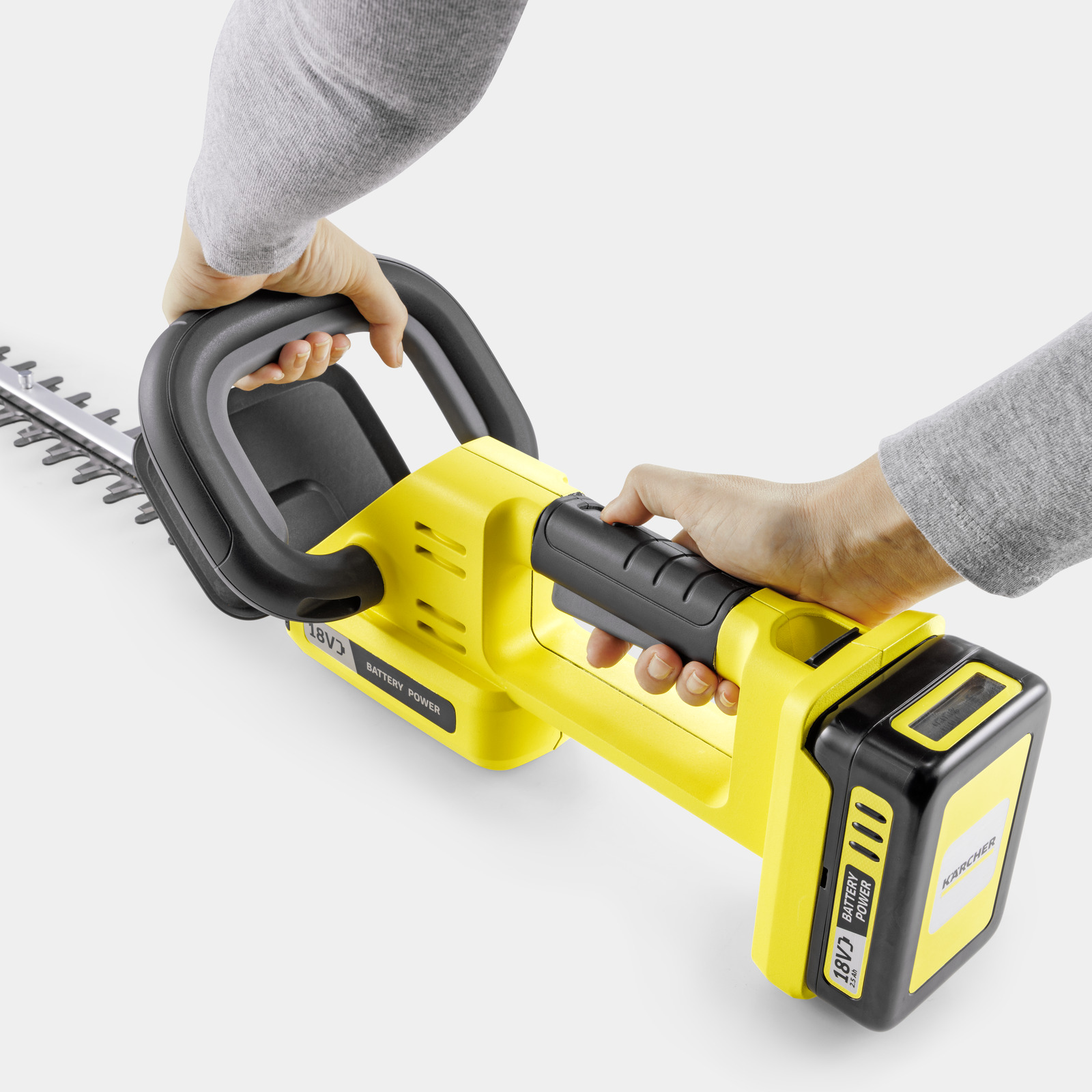 Helle gelbe Heckenschere mit schwarzem Griff und Batteriepack, von Händen gehalten.