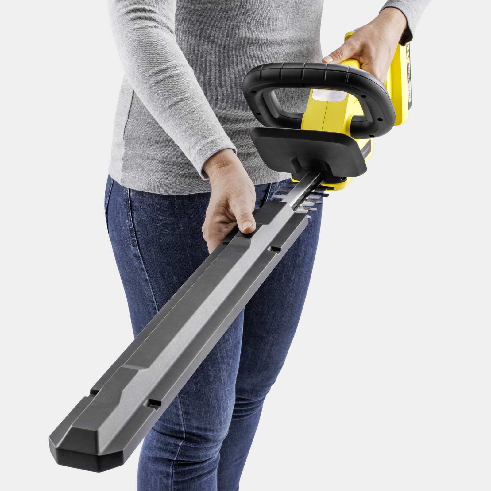 Person mit gelbem Heckenschneider und dunkelblauer Jeans.