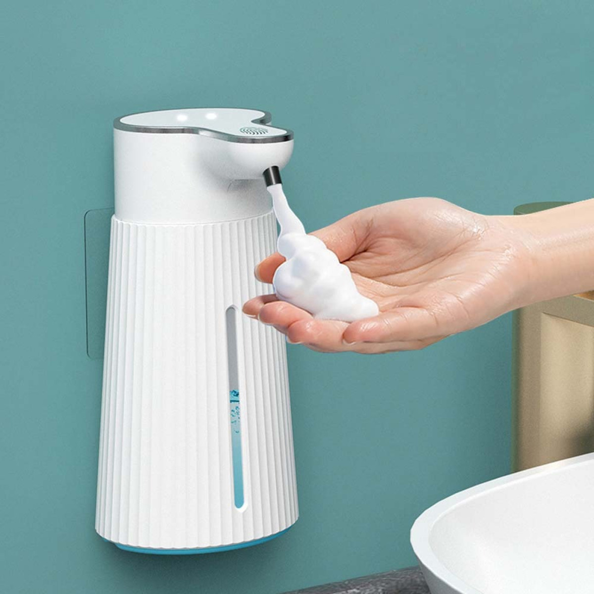 Ein weißer automatischer Seifenspender an einer teal Wand gibt Schaum in eine Hand ab.