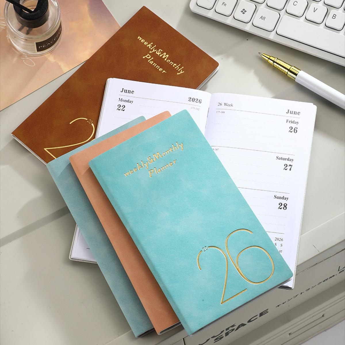 Mehrere Notizbücher in Braun, Rosa und Türkis liegen auf einem Schreibtisch.