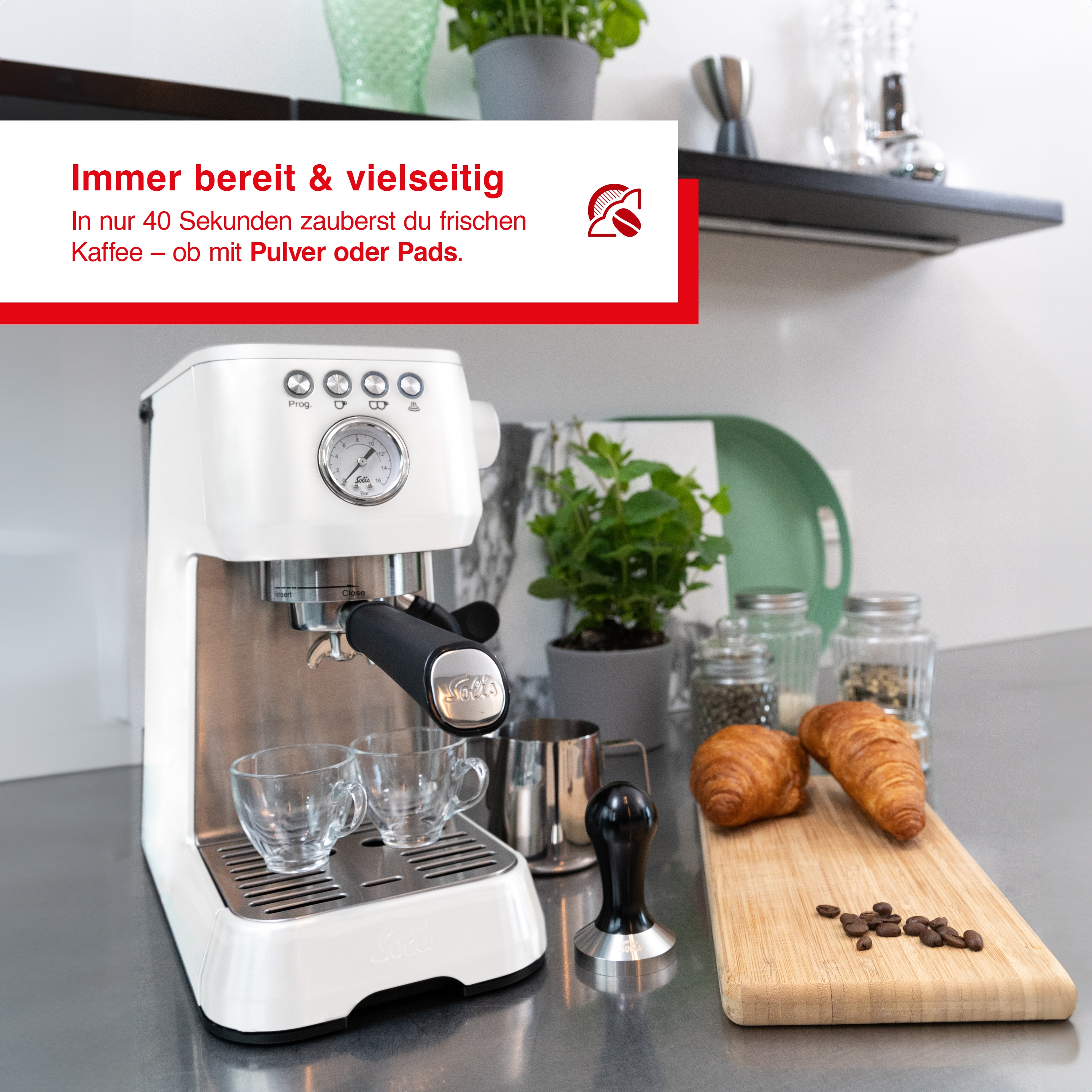 Weiße Kaffeemaschine mit zwei Gläsern, Croissants und Kaffeebohnen.