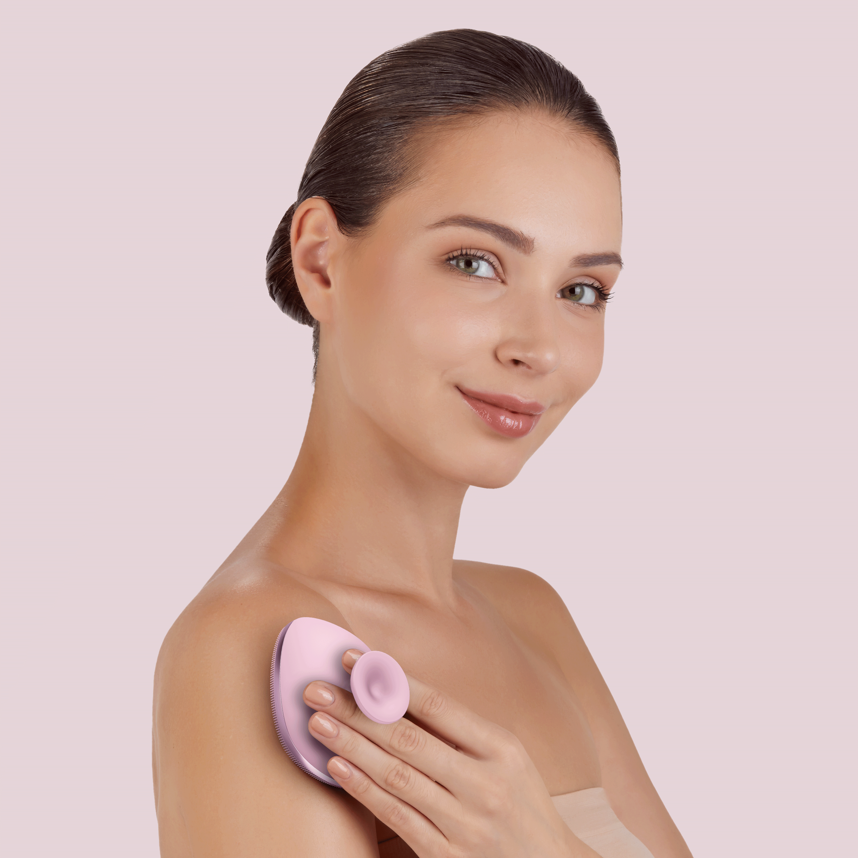 Koyu saçlı bir kadın, pembe yüz temizleme cihazını omzuna tutuyor.