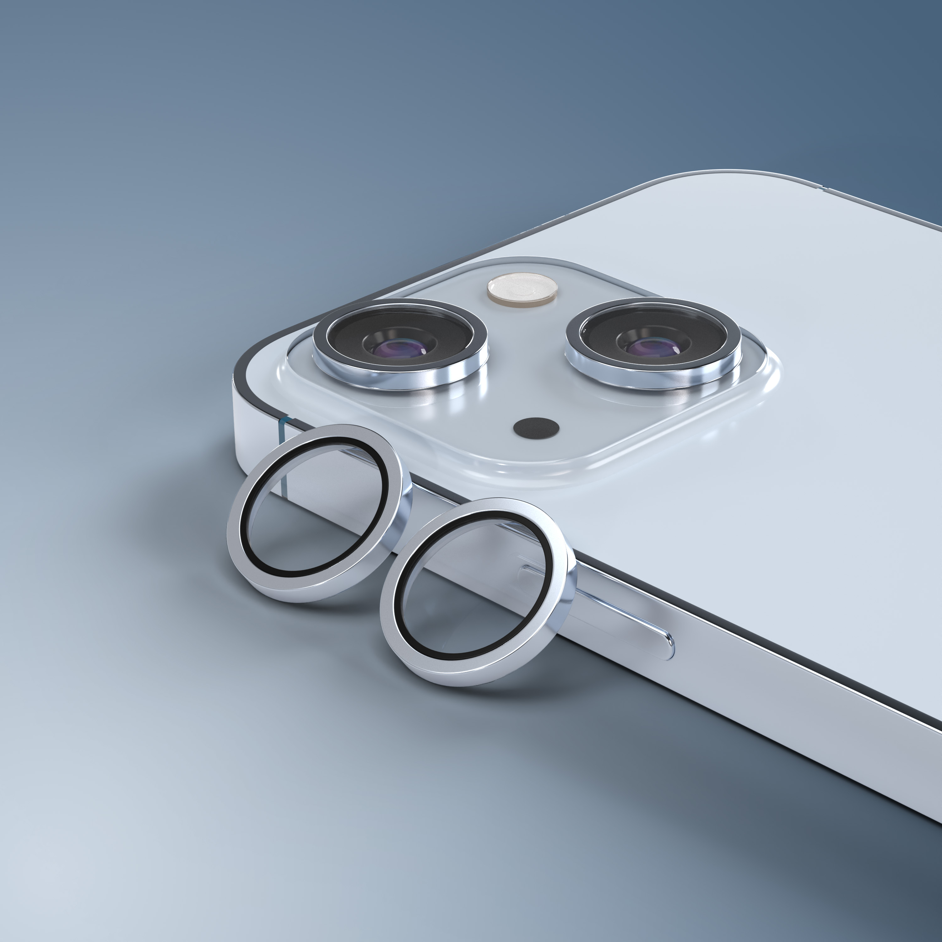 Due anelli protettivi per obiettivo della fotocamera argentati giacciono accanto a uno smartphone bianco.