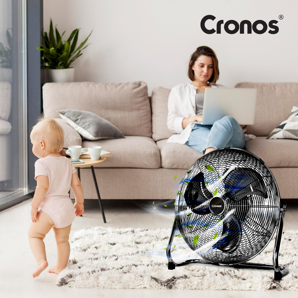 Dziecko raczkuje na dywanie, kobieta pracuje na laptopie, wentylator dmucha.