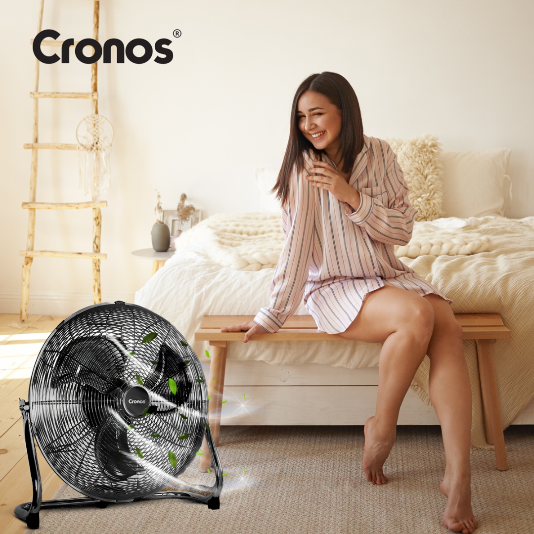 Czarny wentylator z obracającymi się łopatkami stoi przed łóżkiem.